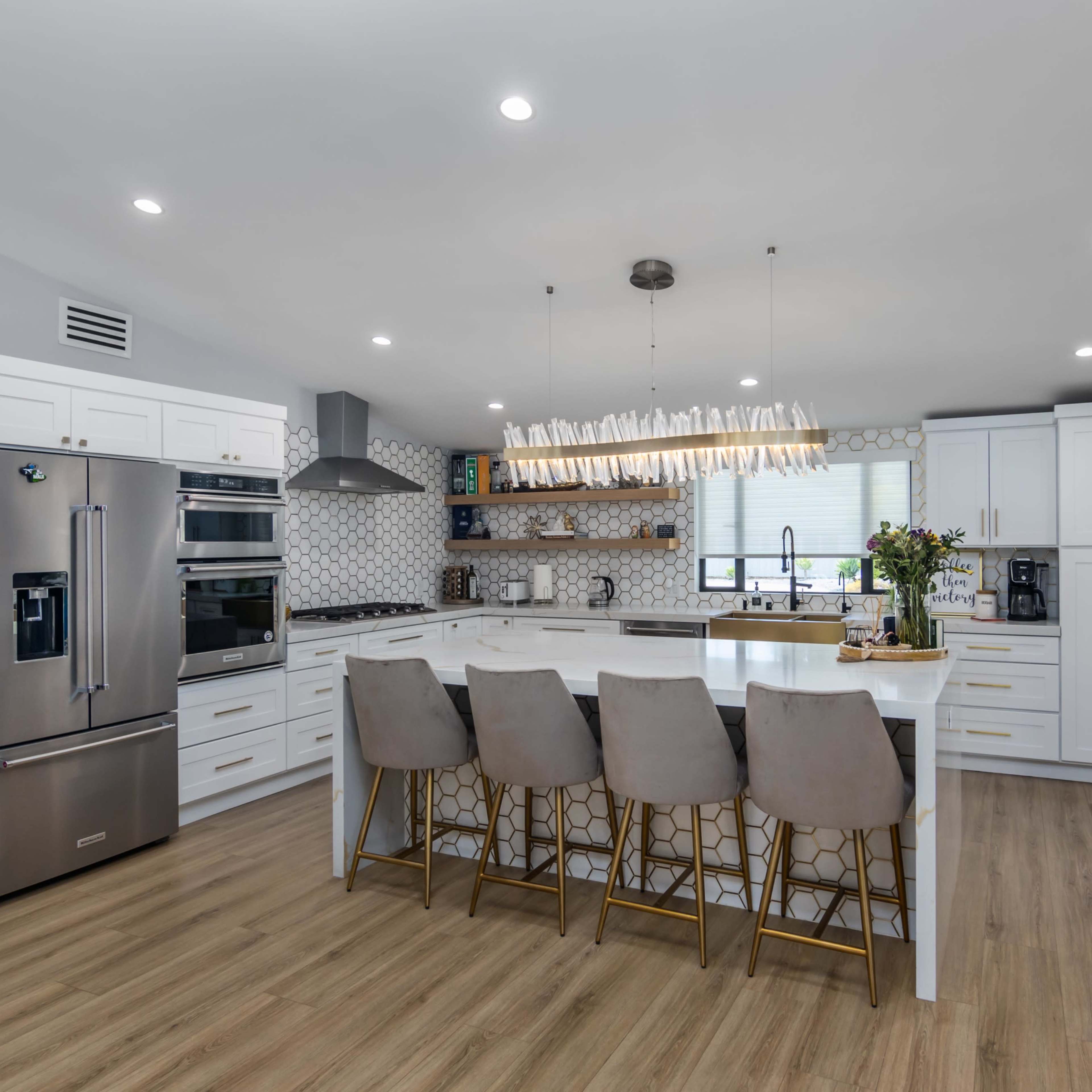 A modern kitchen features a central island with seating, stainless steel appliances, and white cabinetry with a patterned backsplash.