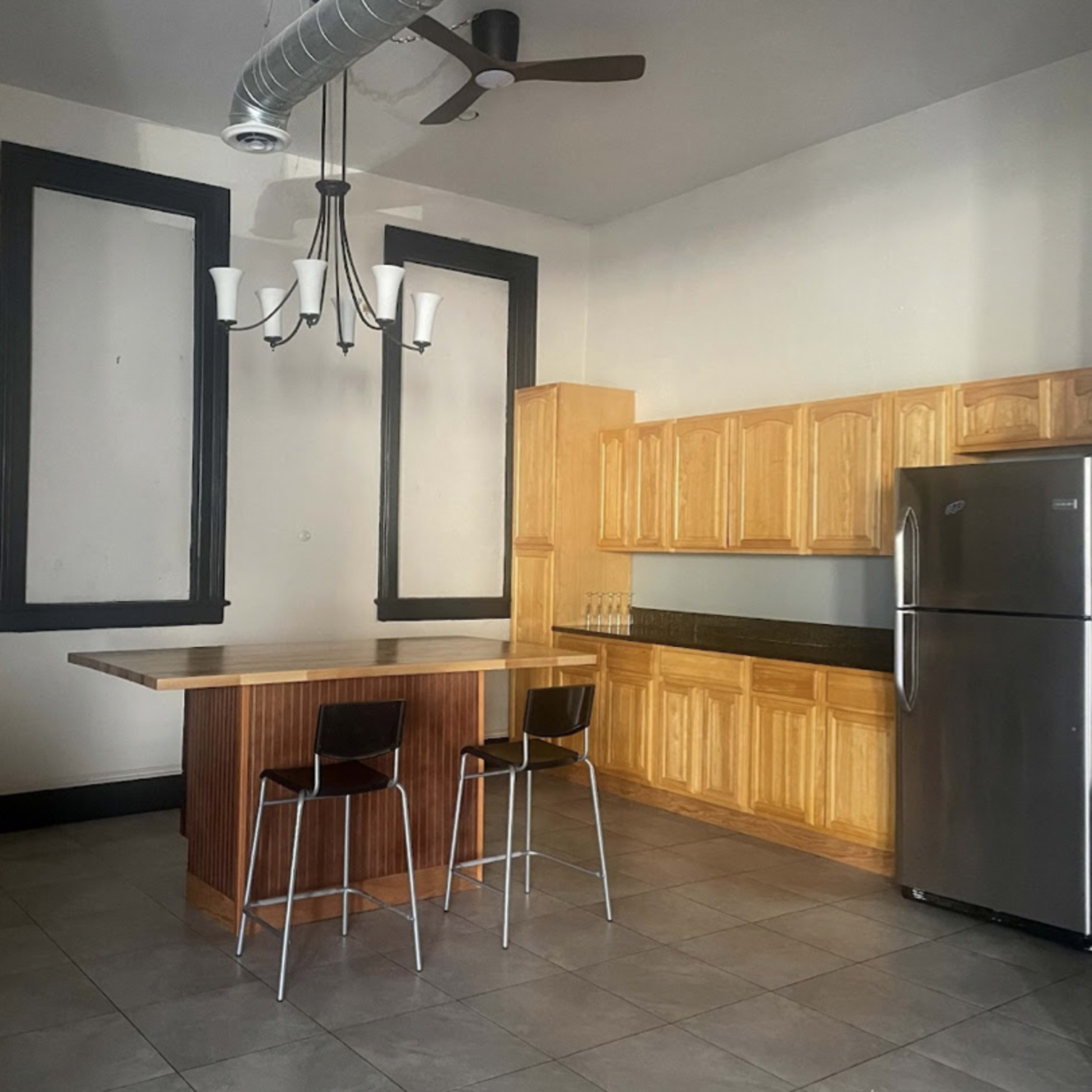 A spacious kitchen with a wooden island, two stools, a stainless steel refrigerator, and cabinetry against the wall.