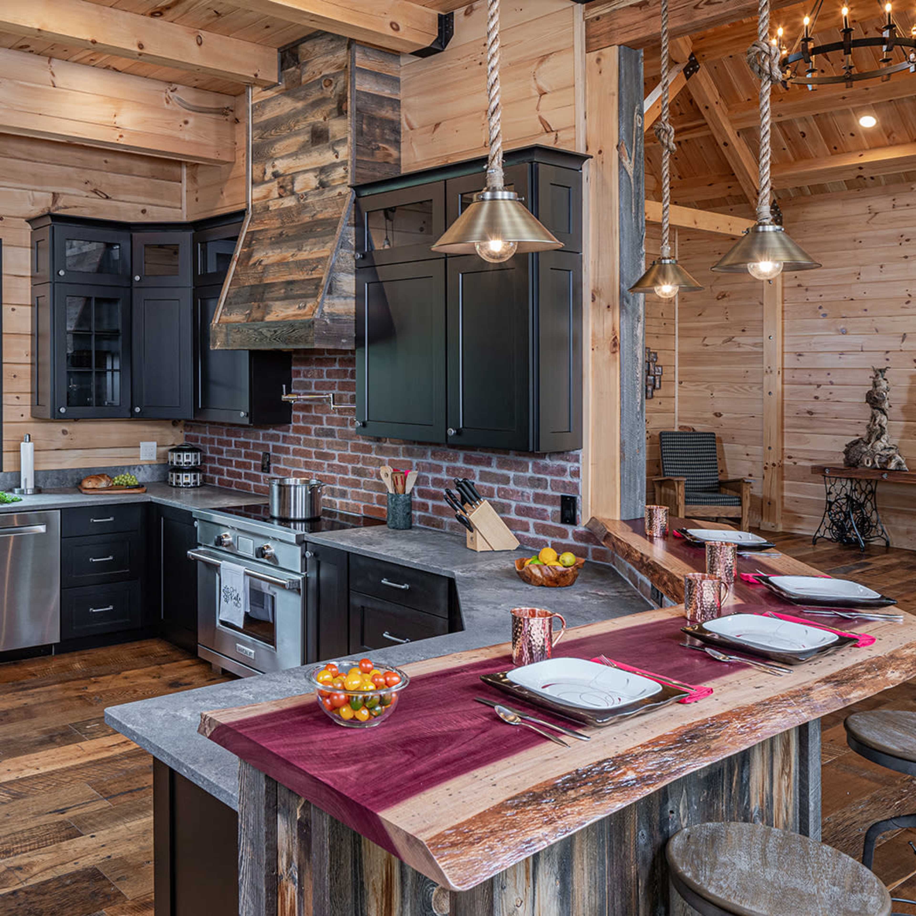 A modern kitchen with black cabinets, a stainless steel stove, and a rustic wooden island, surrounded by wooden walls and a large window that offers a view of the outdoors.