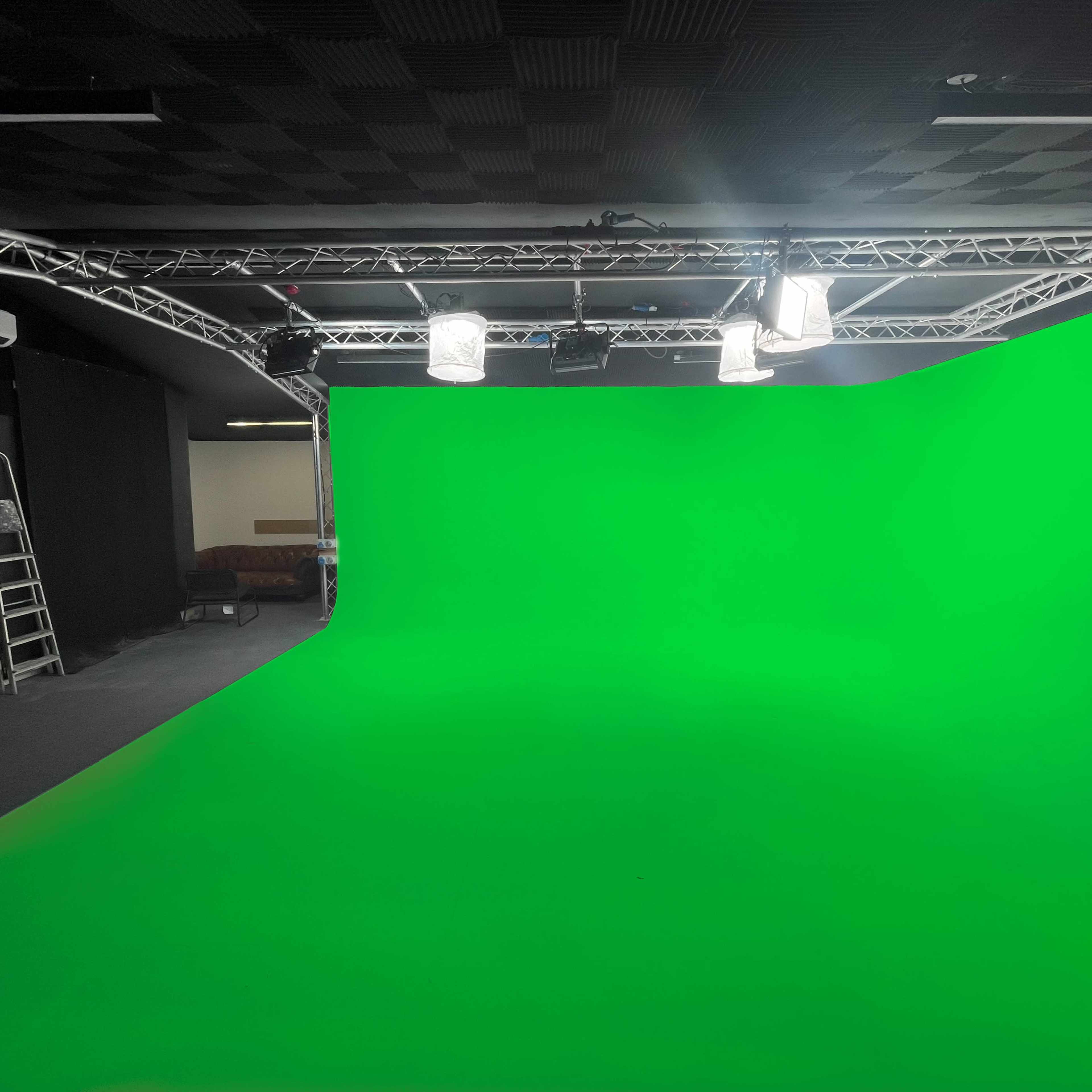 A green screen studio with lighting supports and a ladder against the wall.
