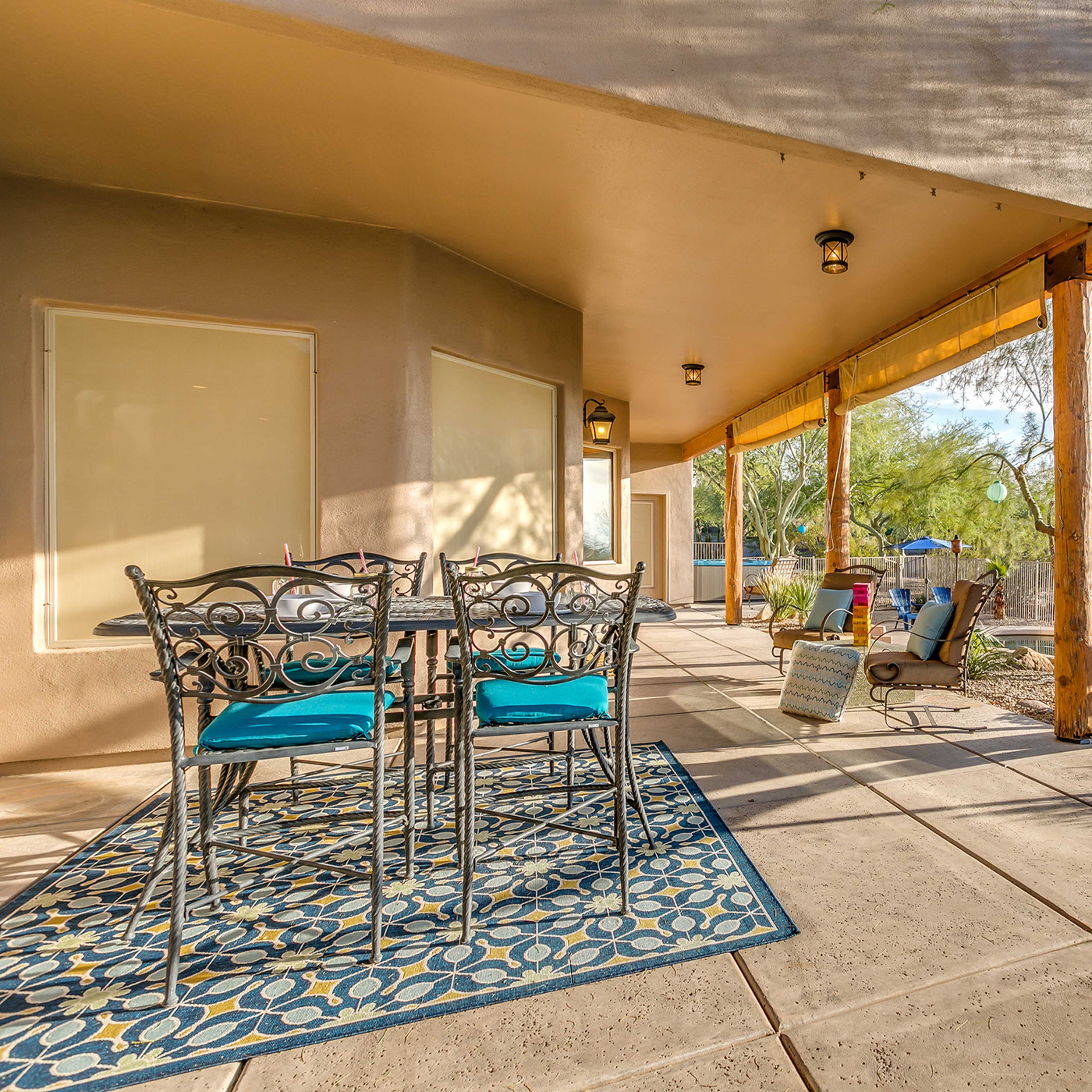 A patio area with a table and chairs, bordered by desert landscaping and shaded by a building.