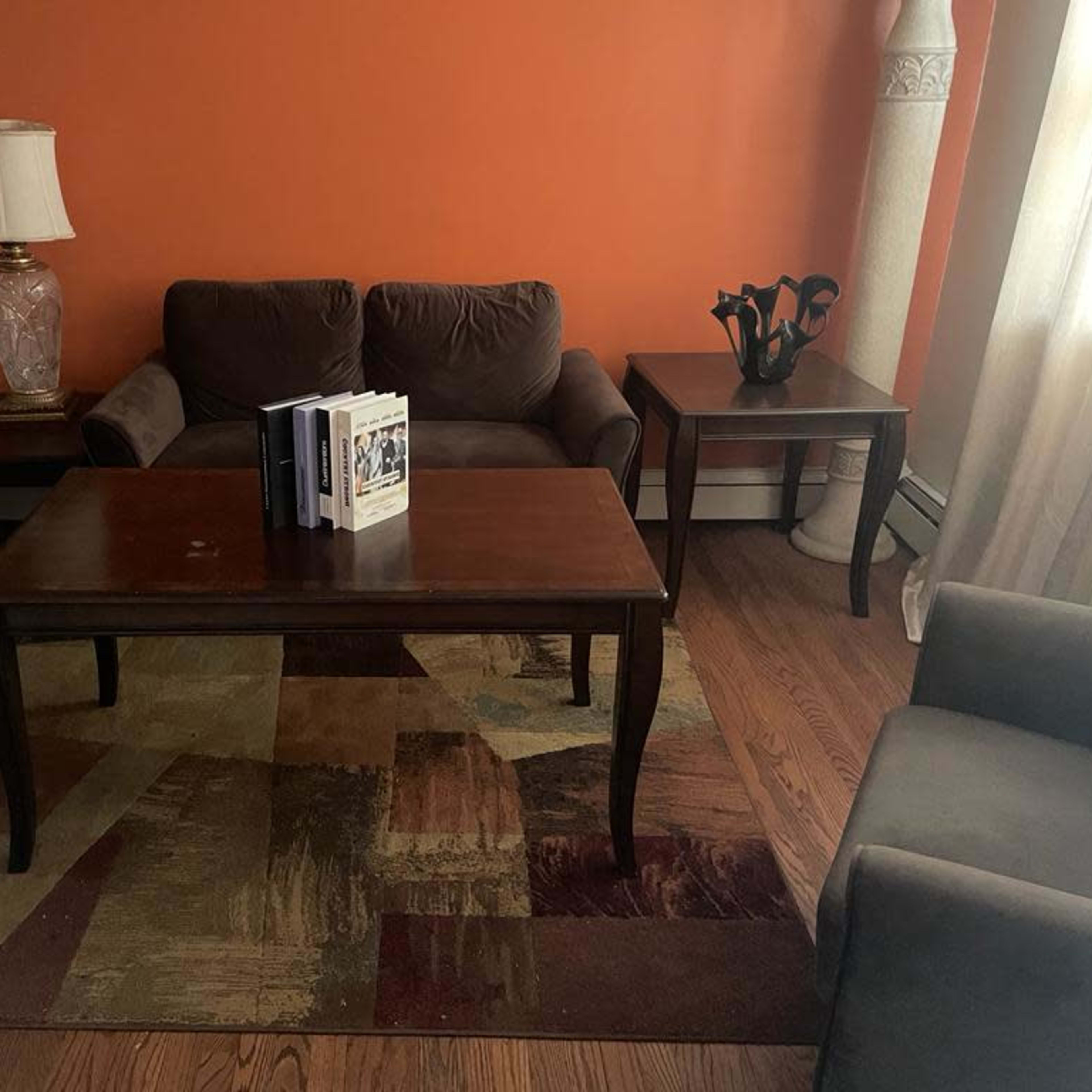 A living room with an orange wall, a wooden table, four chairs, a lamp, and a book on the table.