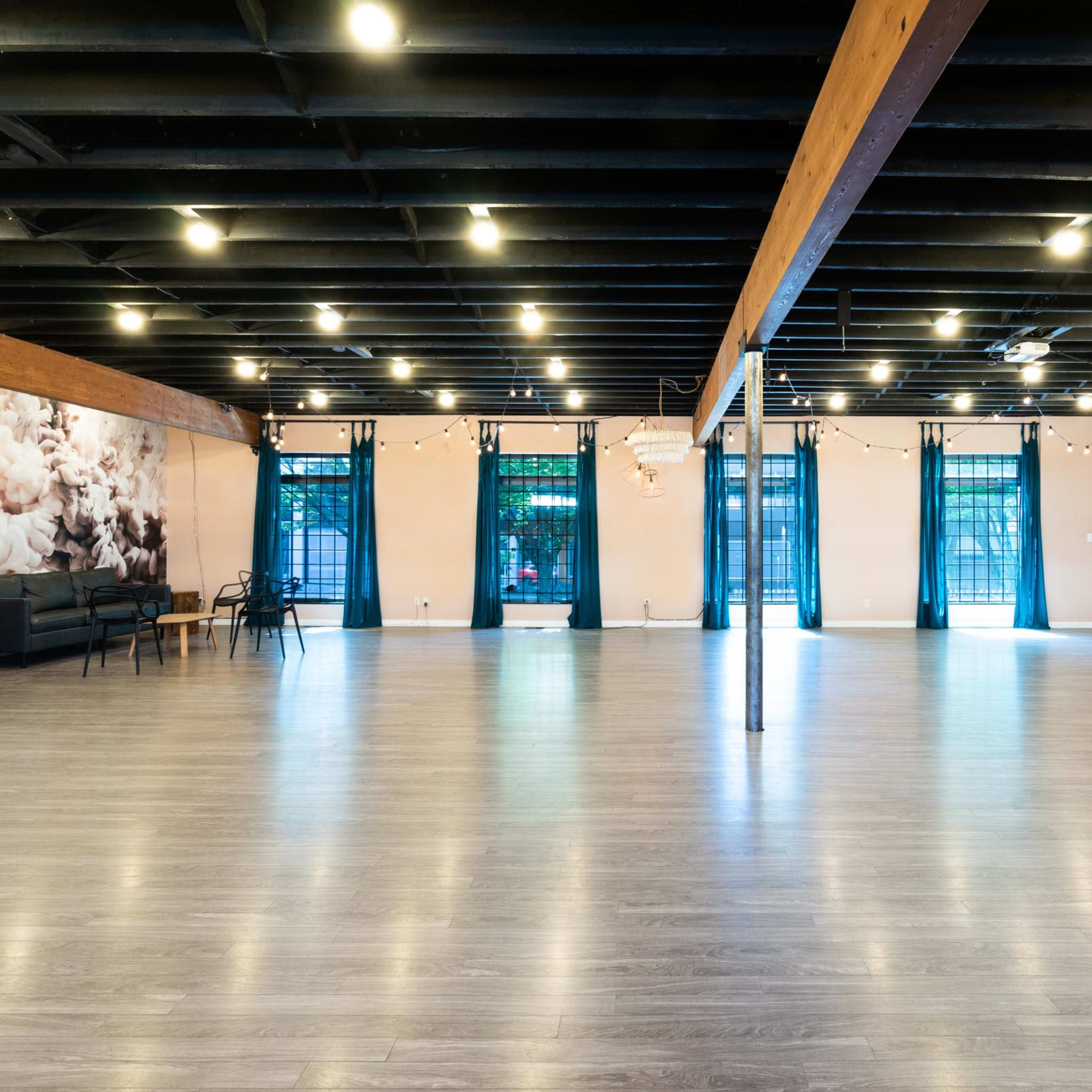 A spacious interior with wooden beams, polished gray flooring, and large windows, illuminated by overhead lights.