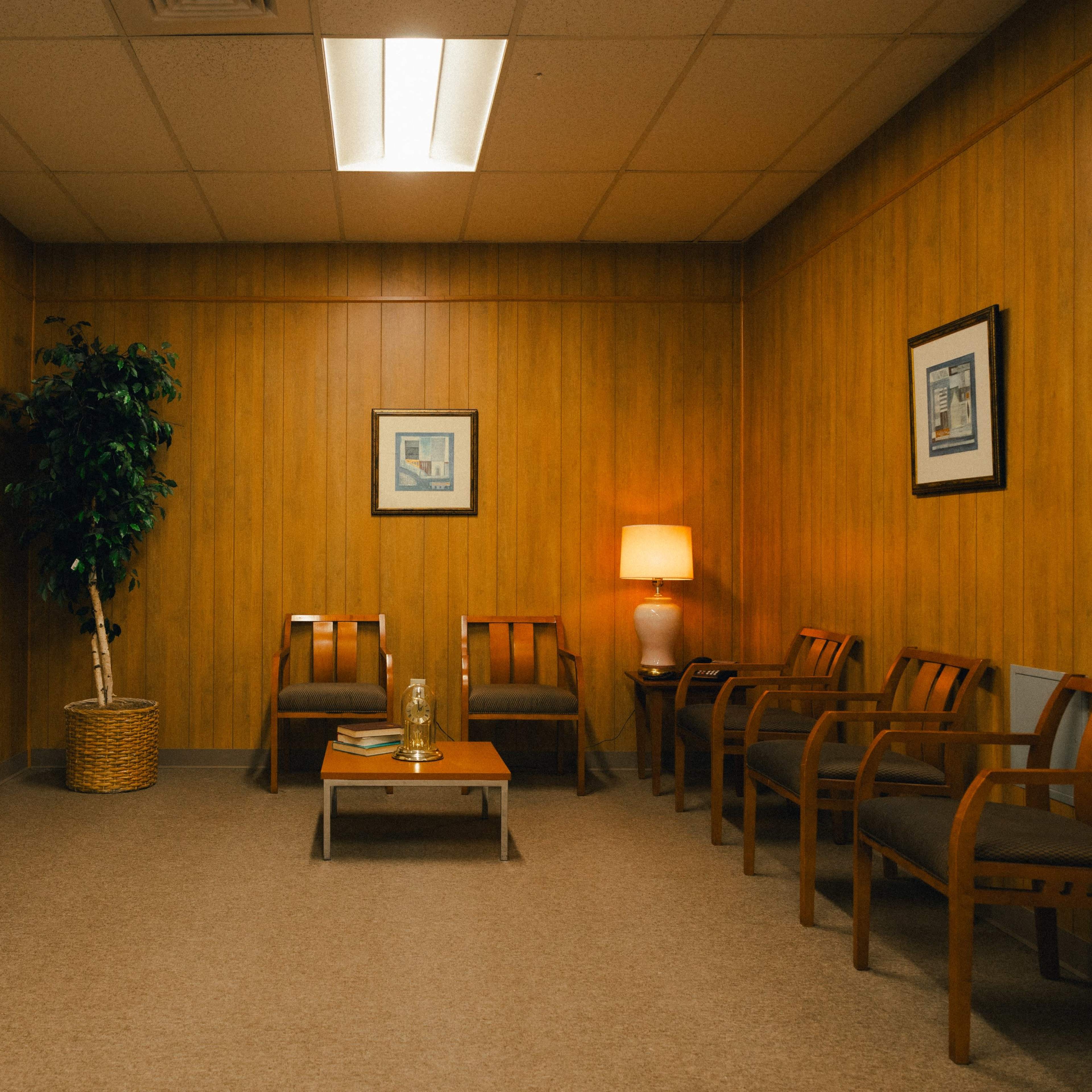 A waiting room with wooden-paneled walls, a water cooler, several chairs, a small table, and framed pictures on the walls.