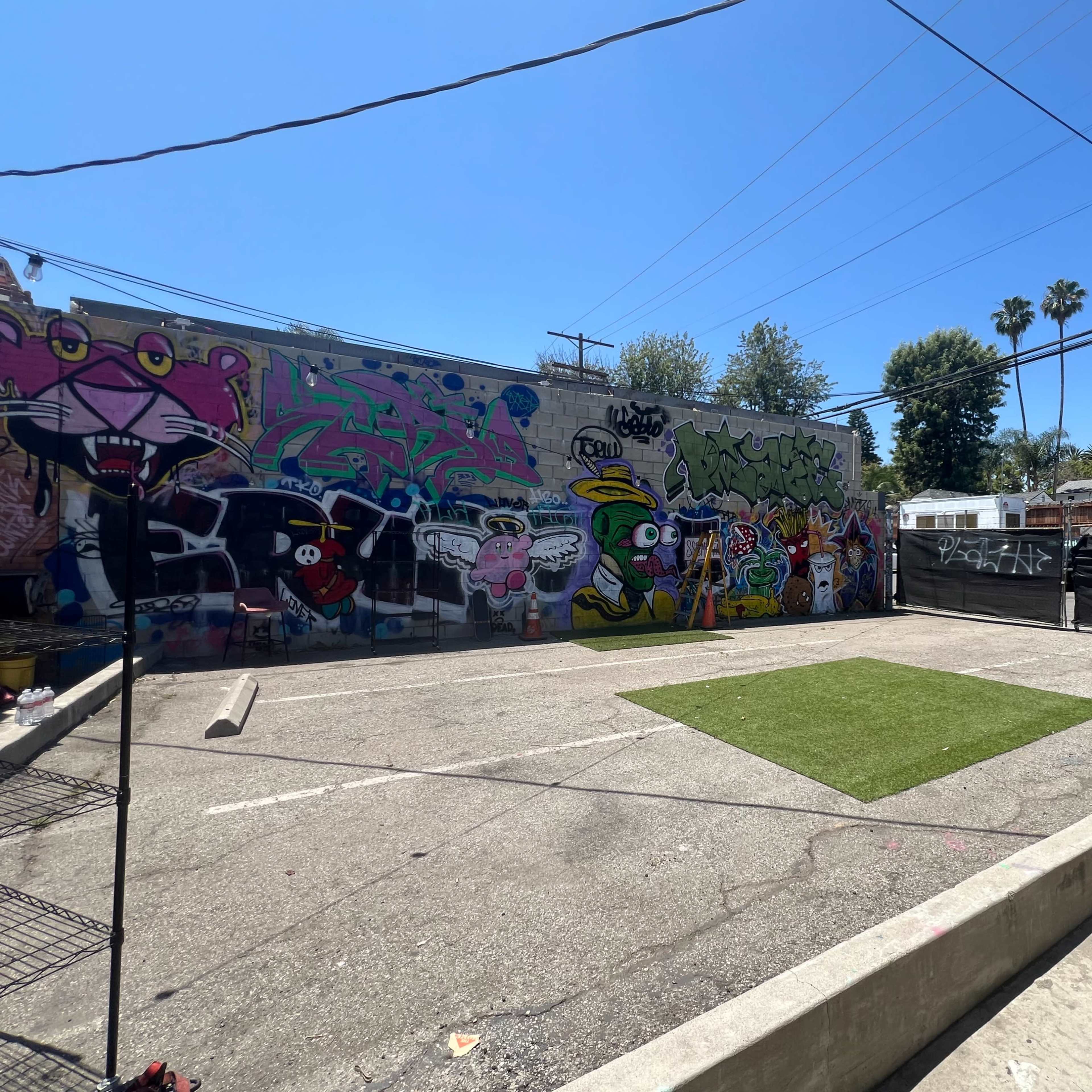A concrete courtyard with a patch of artificial grass and a vibrant graffiti-covered wall in the background.