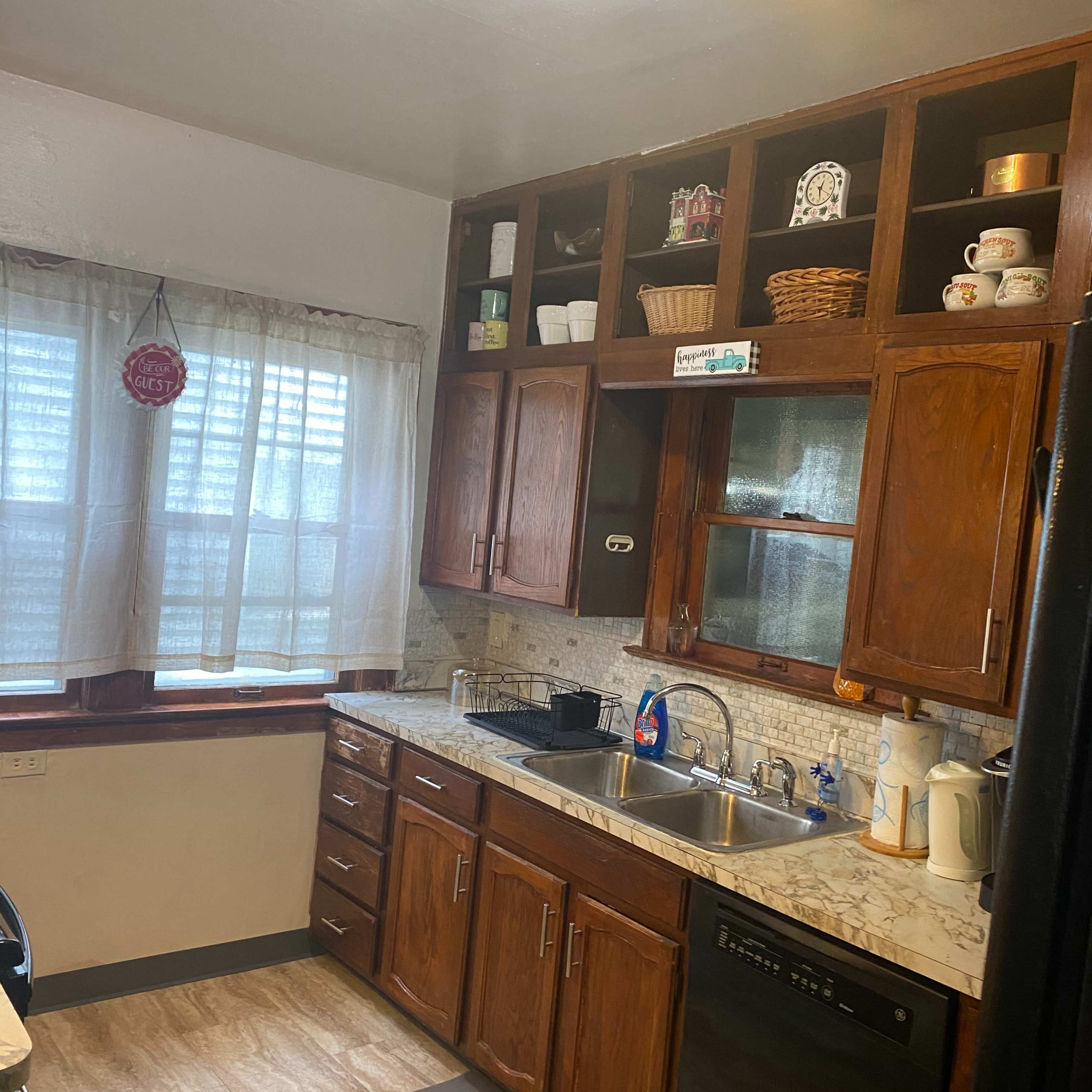 A kitchen with wooden cabinets, a sink, and a window adorned with sheer curtains.