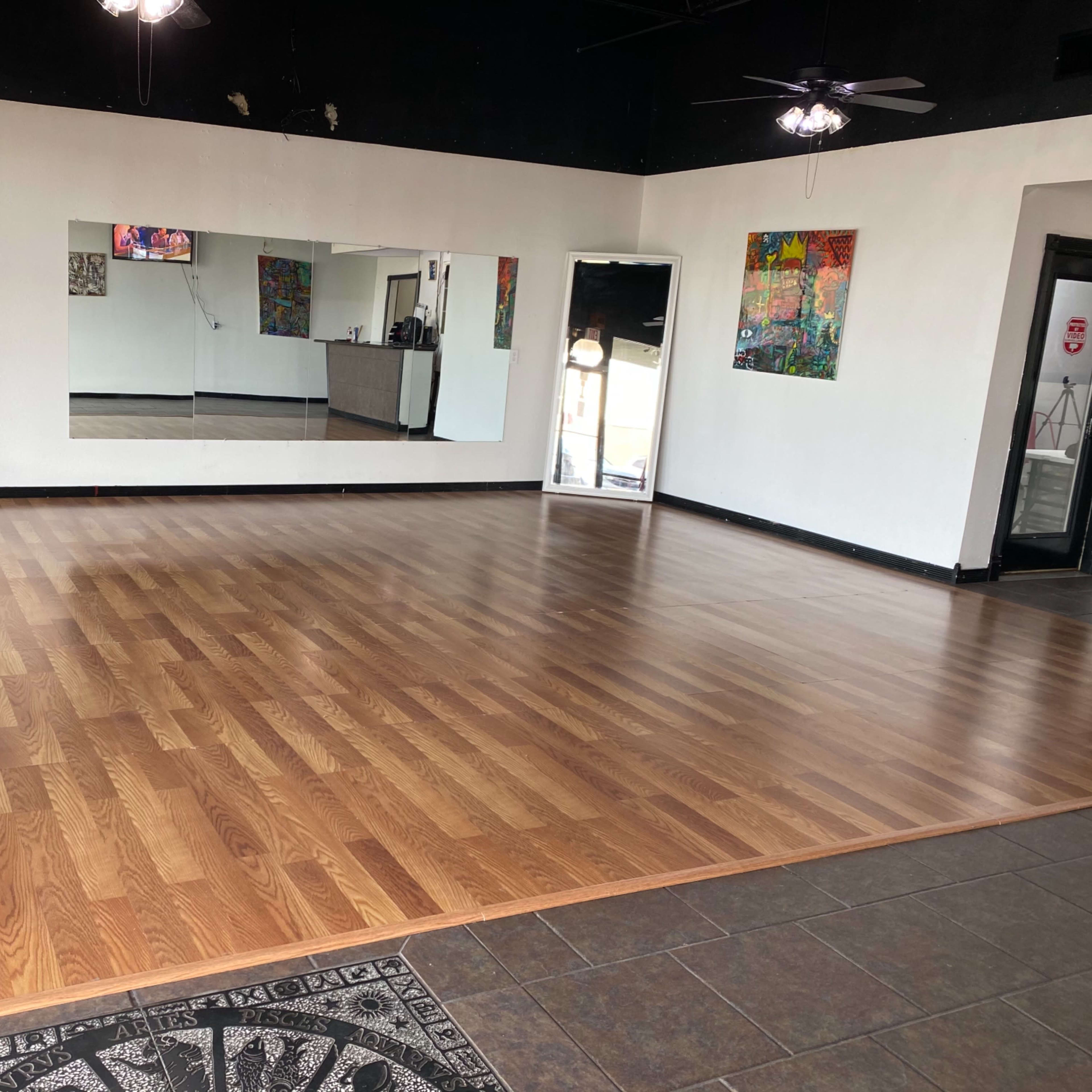A spacious, empty room with wooden flooring, mirrors on one wall, and colorful artwork displayed.