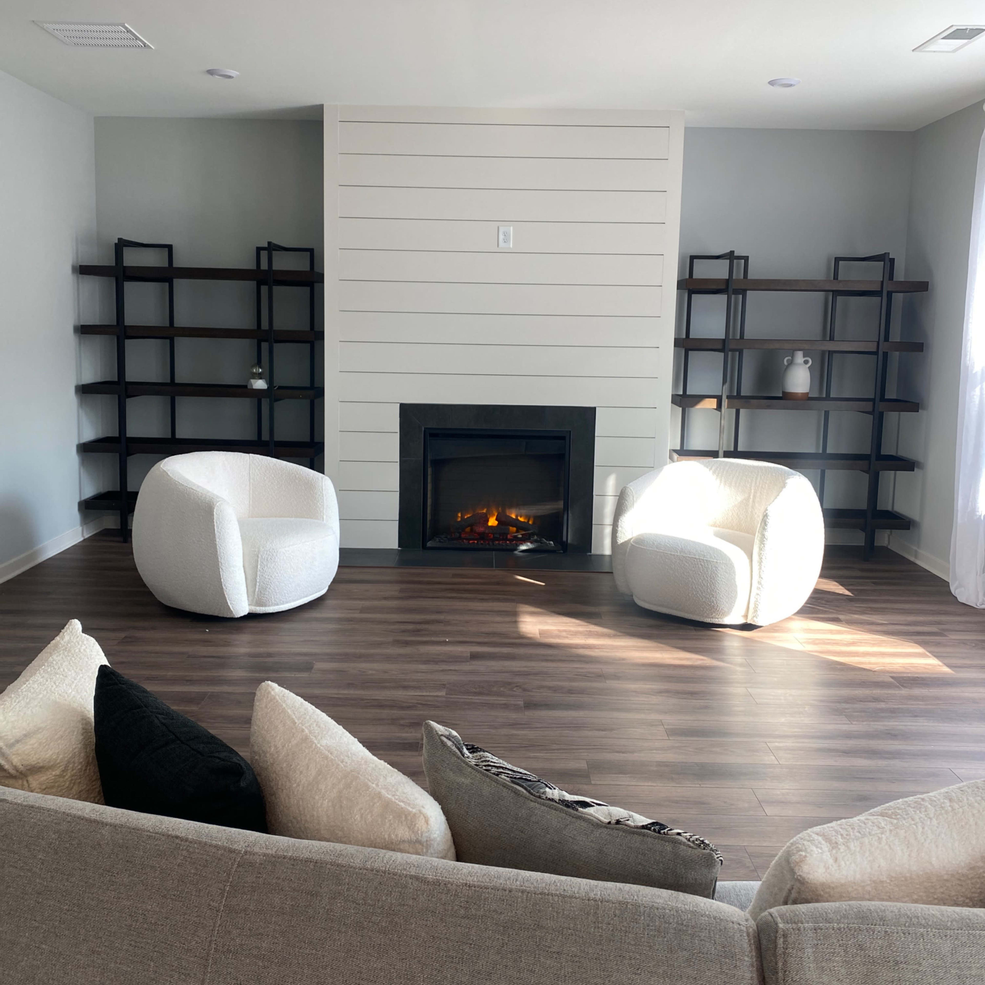 A modern living room featuring a central fireplace flanked by two round white chairs and dark wooden bookshelves against a light-colored wall.