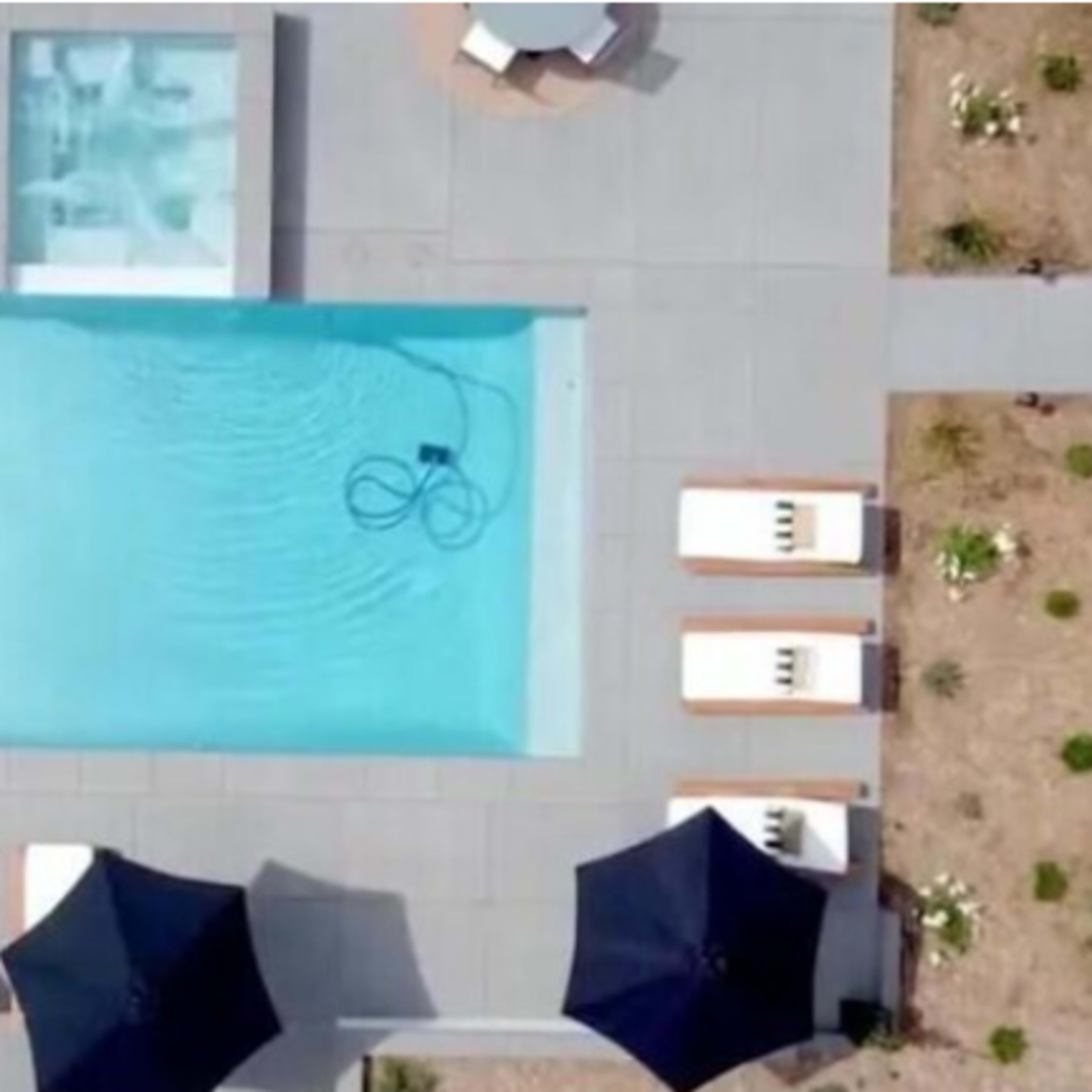 An aerial view of a modern swimming pool surrounded by loungers and patio furniture in a landscaped area.