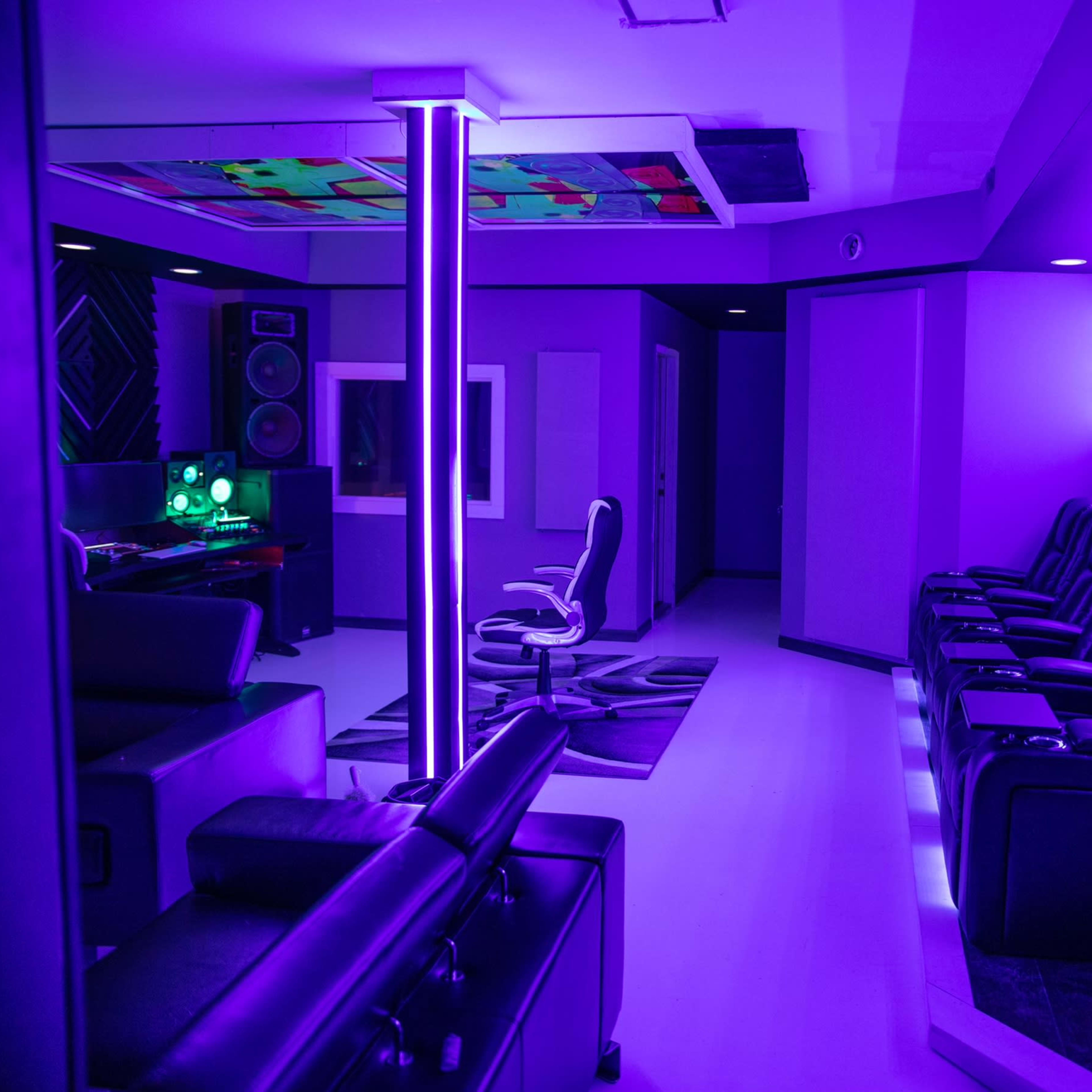A modern room with purple lighting, featuring black reclining chairs, a large screen, and a sleek workspace area.