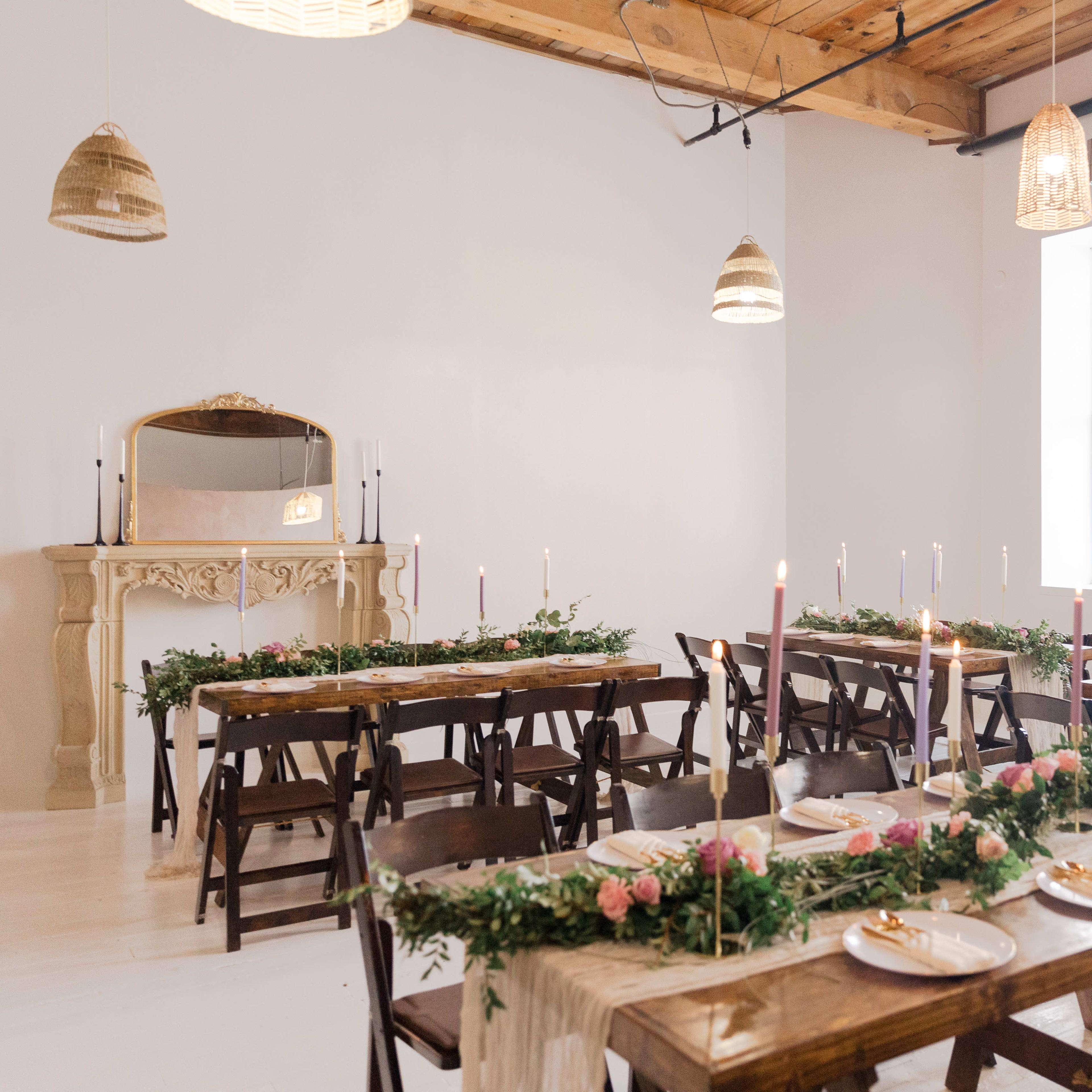 A spacious dining area features wooden tables set with plates, candles, and floral centerpieces against a plain white wall and a decorative mirror.