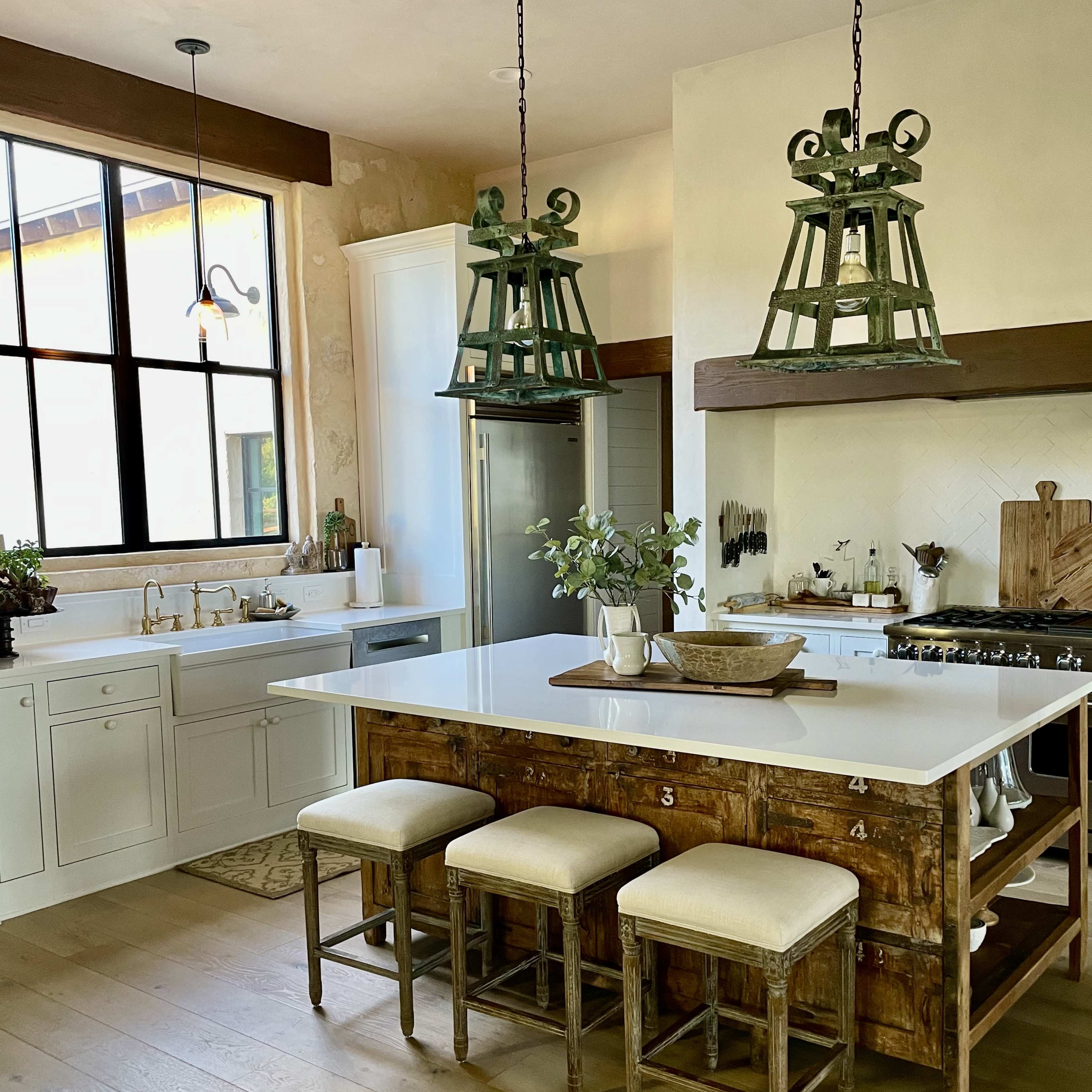 The kitchen features a large island with wooden stools, industrial-style pendant lights, and a well-organized countertop.