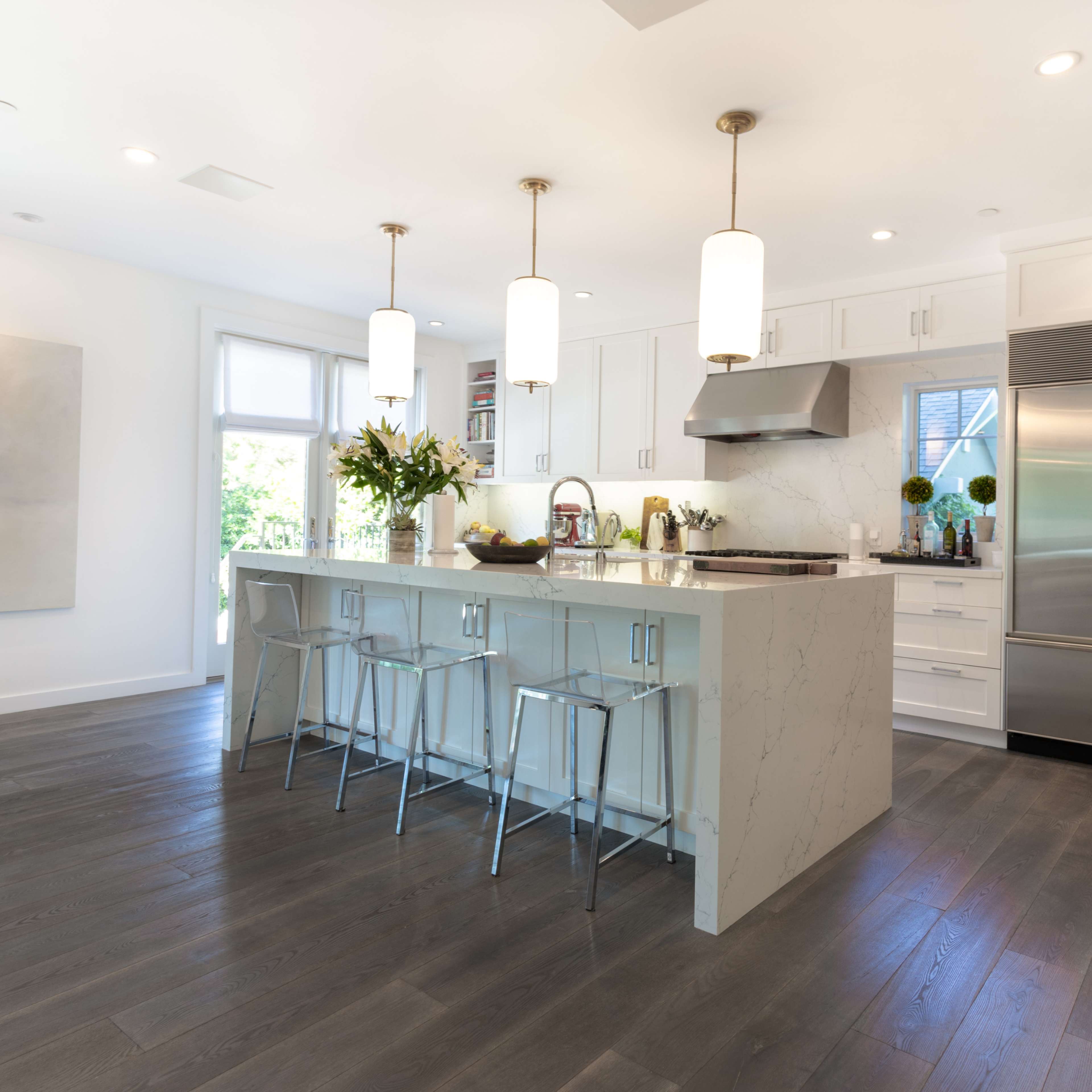 A modern kitchen with a large island, stainless steel appliances, and pendant lights hanging above barstool seating.