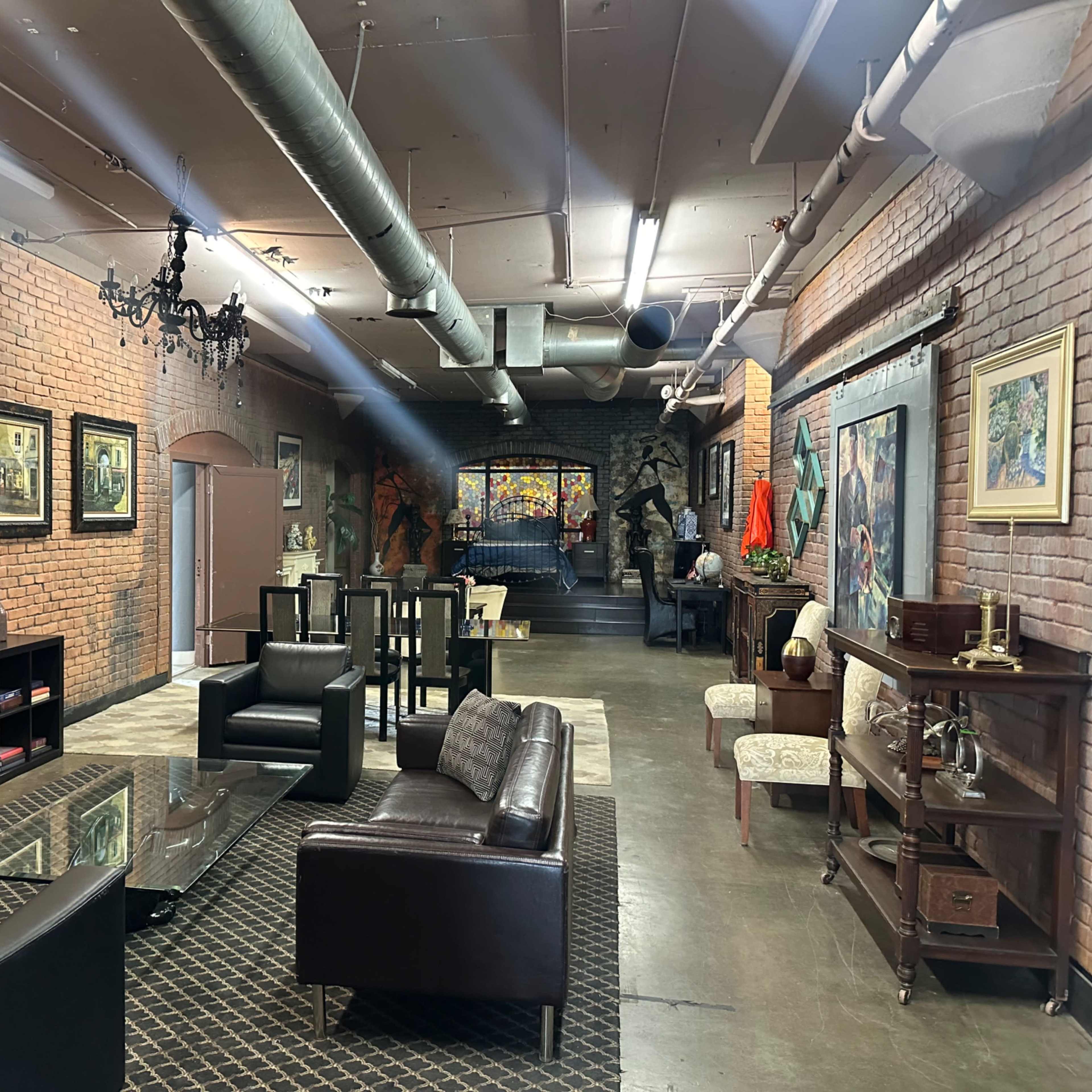 A spacious, industrial-style lounge area with exposed brick walls, a television, modern furniture, and various artworks displayed on the walls.