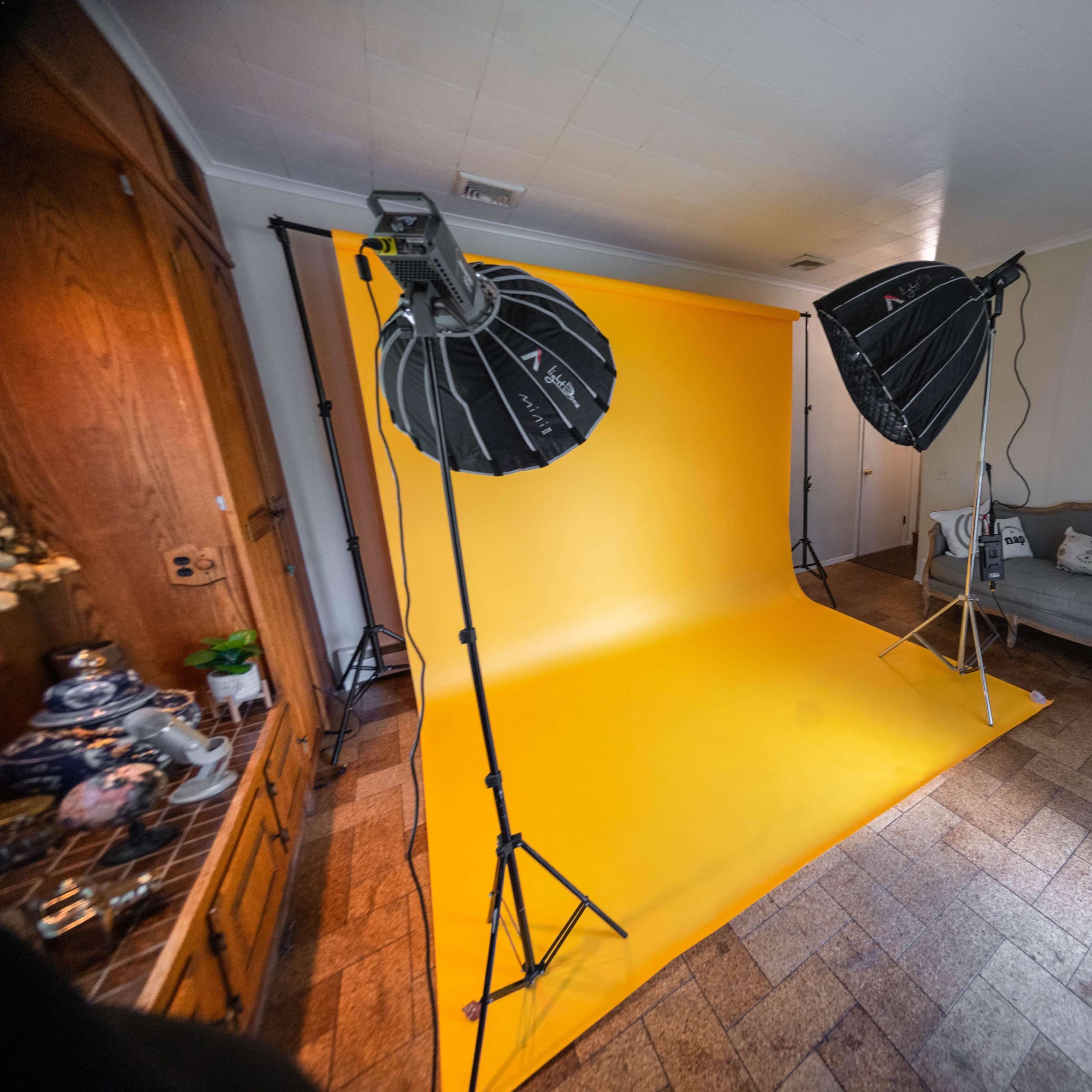 A photography setup featuring two studio lights positioned toward a yellow backdrop in a room with a wooden cabinet and a couch.