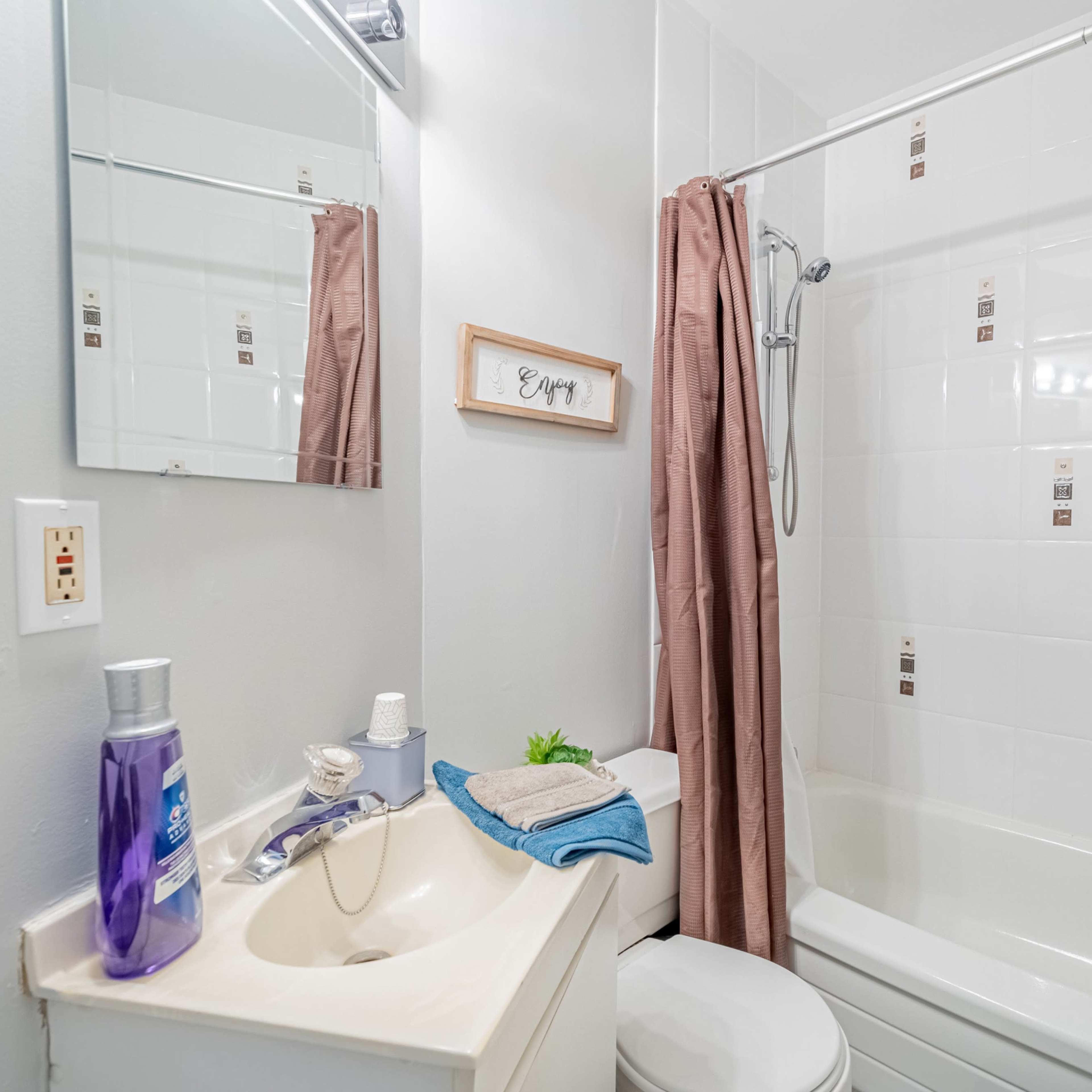 A compact bathroom featuring a sink with toiletries, a toilet, and a shower-tub combination with a curtain.