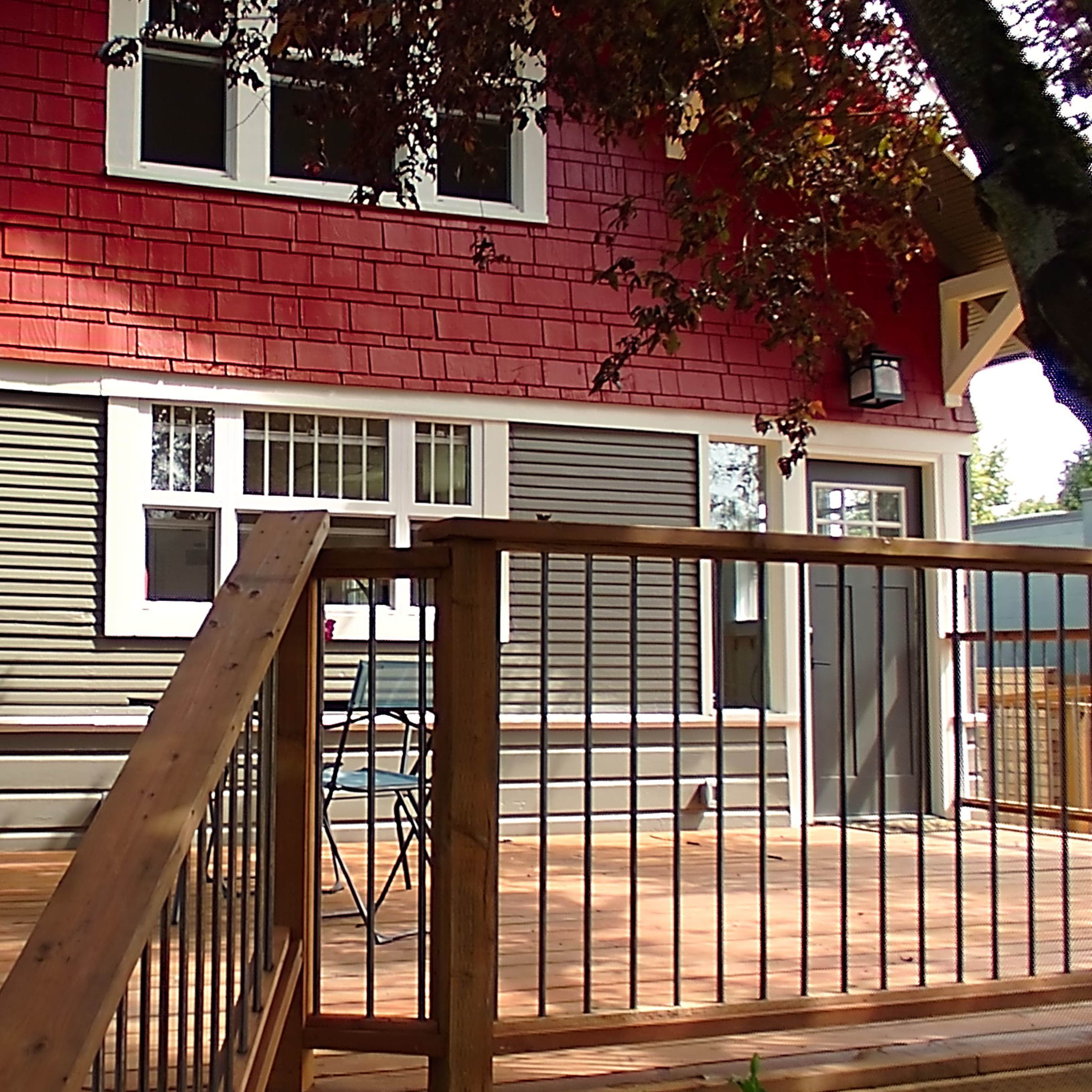 A wooden deck with two black chairs and a small table in front of a red and gray house with multiple windows.