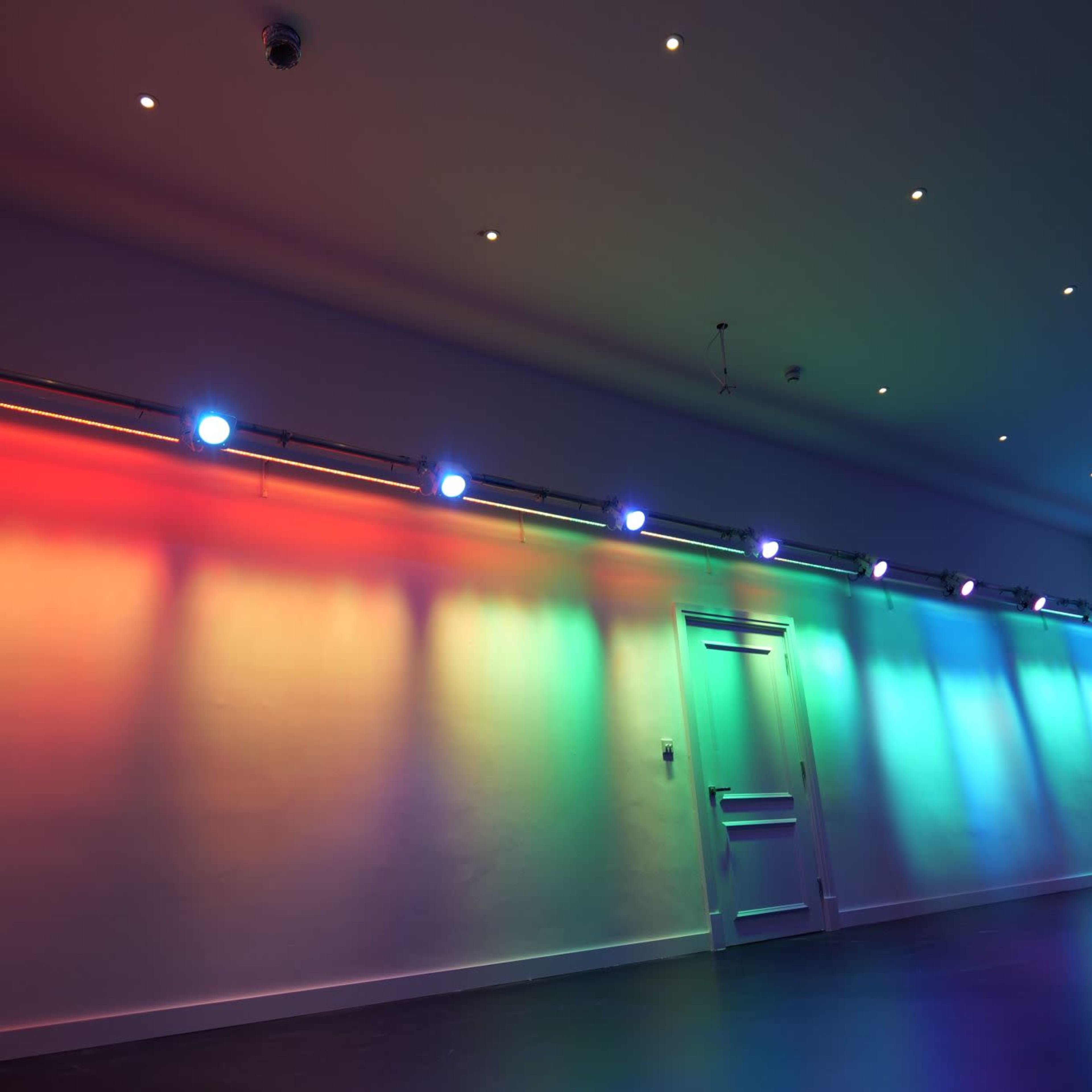 A dimly lit room with colorful lights casting vibrant shadows on the white walls.