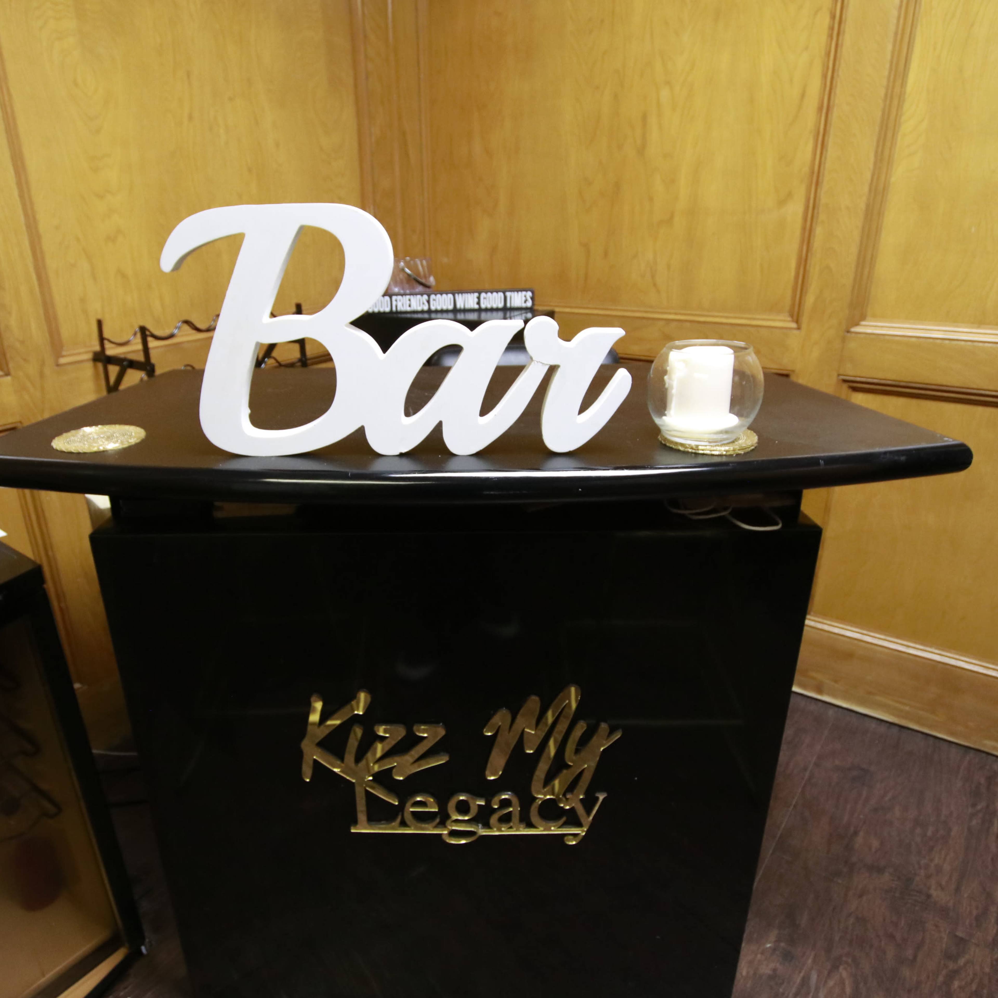 A stylish black bar counter displays a large white sign that reads "Bar" alongside a candle and decorative items.