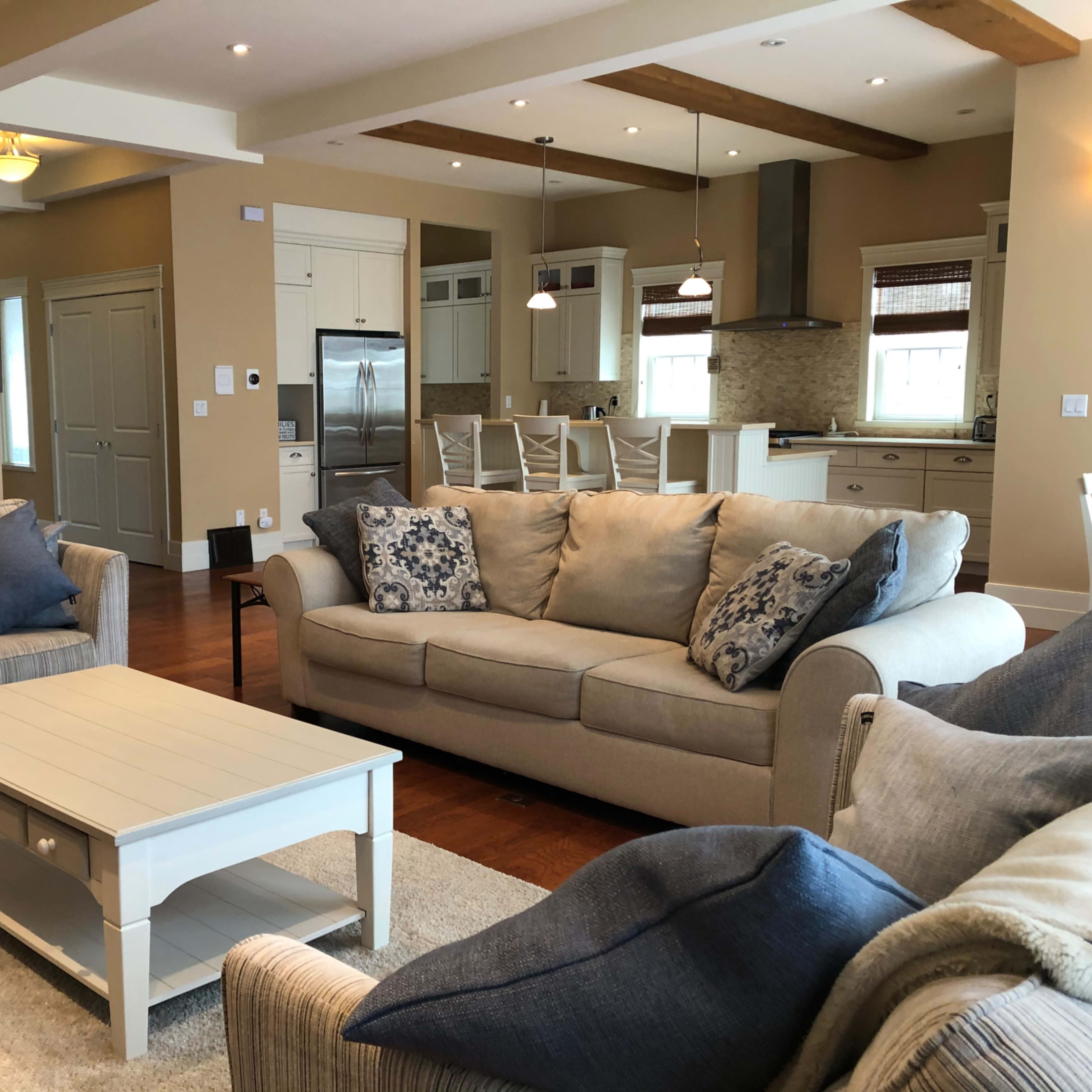 A spacious living room featuring two light-colored sofas, a coffee table, and a kitchen area in the background.