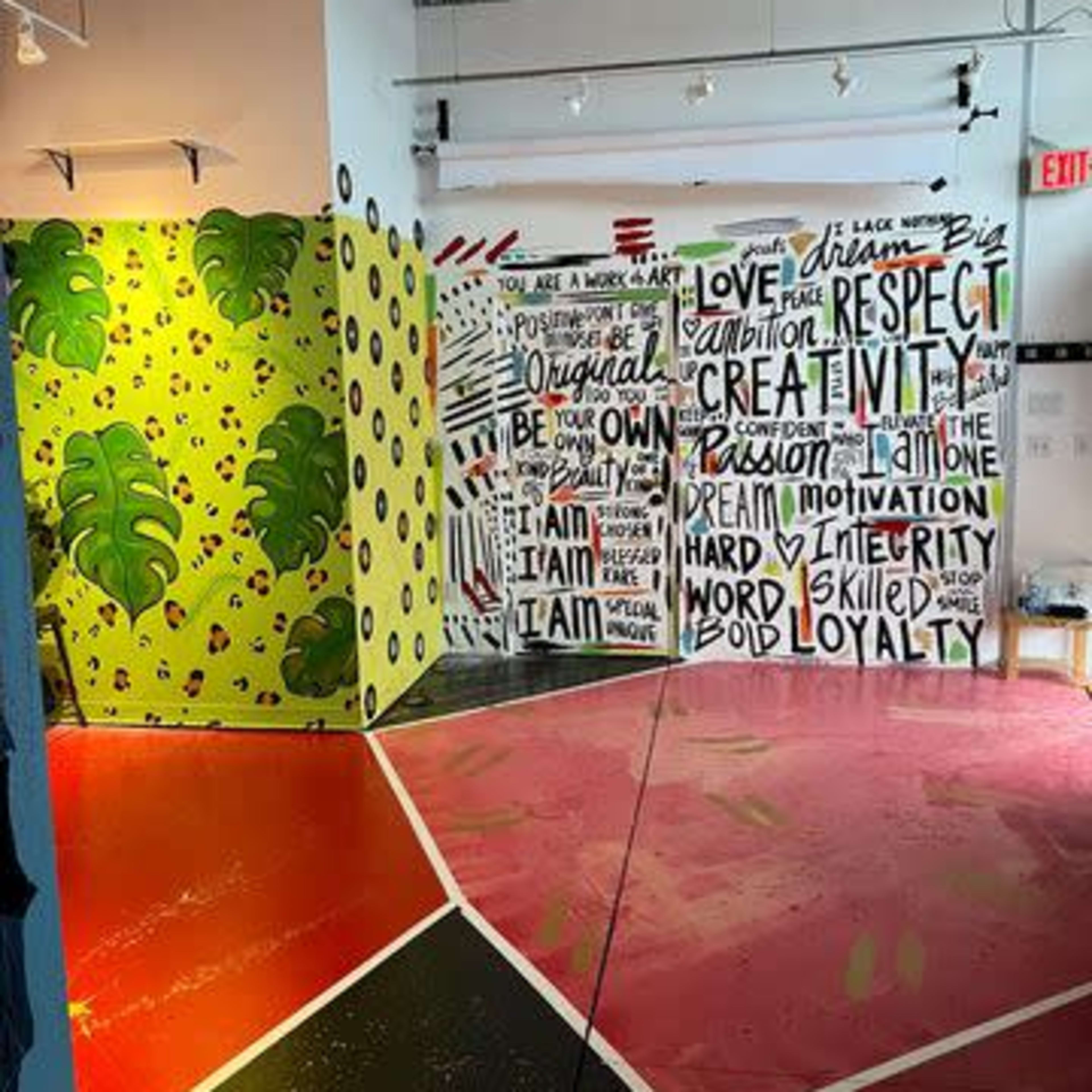 An interior space with vibrant murals and painted walls displaying motivational words and colorful leaf patterns on the opposite wall.