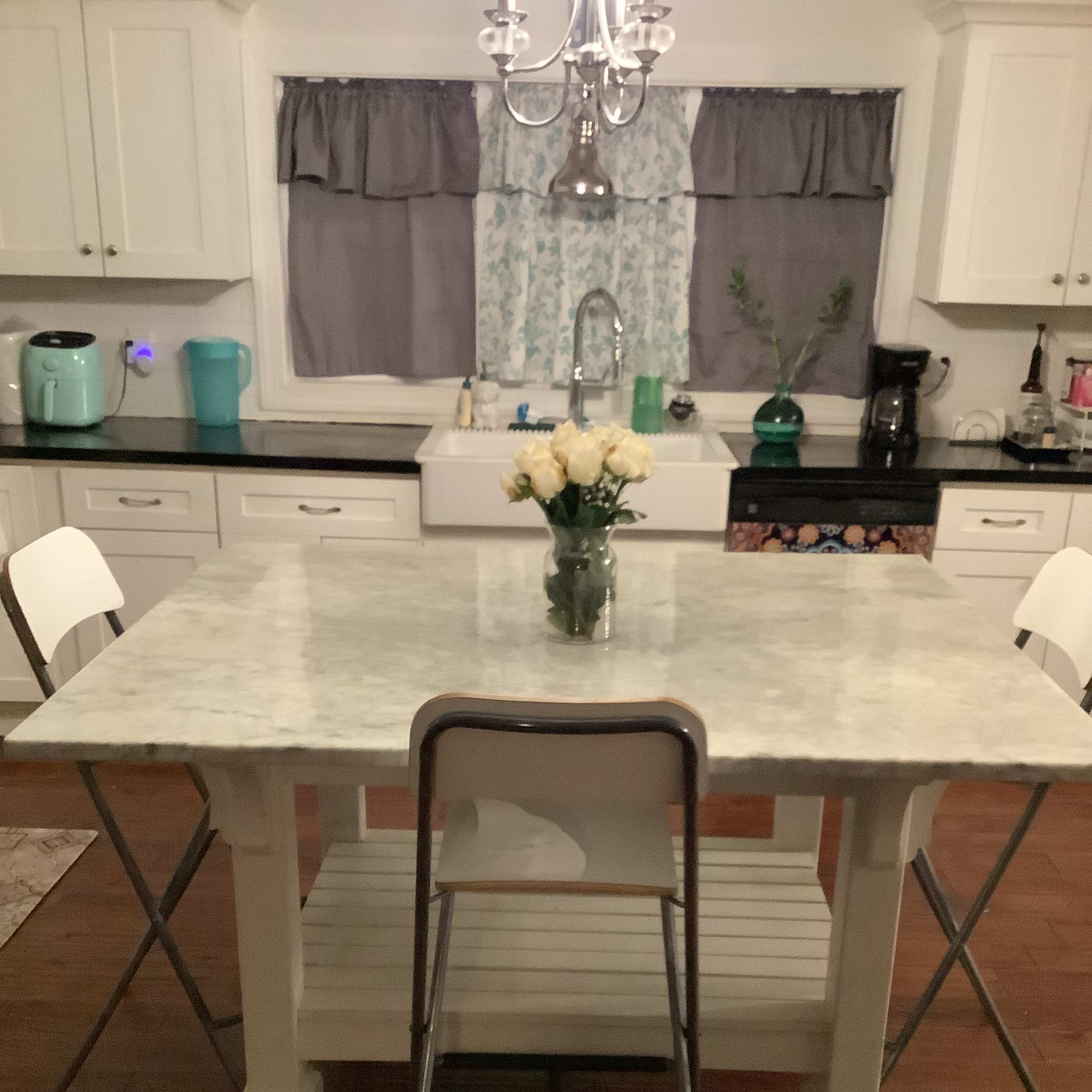 A marble-top table with a vase of flowers is surrounded by four chairs in a kitchen with white cabinetry and dark wood flooring.