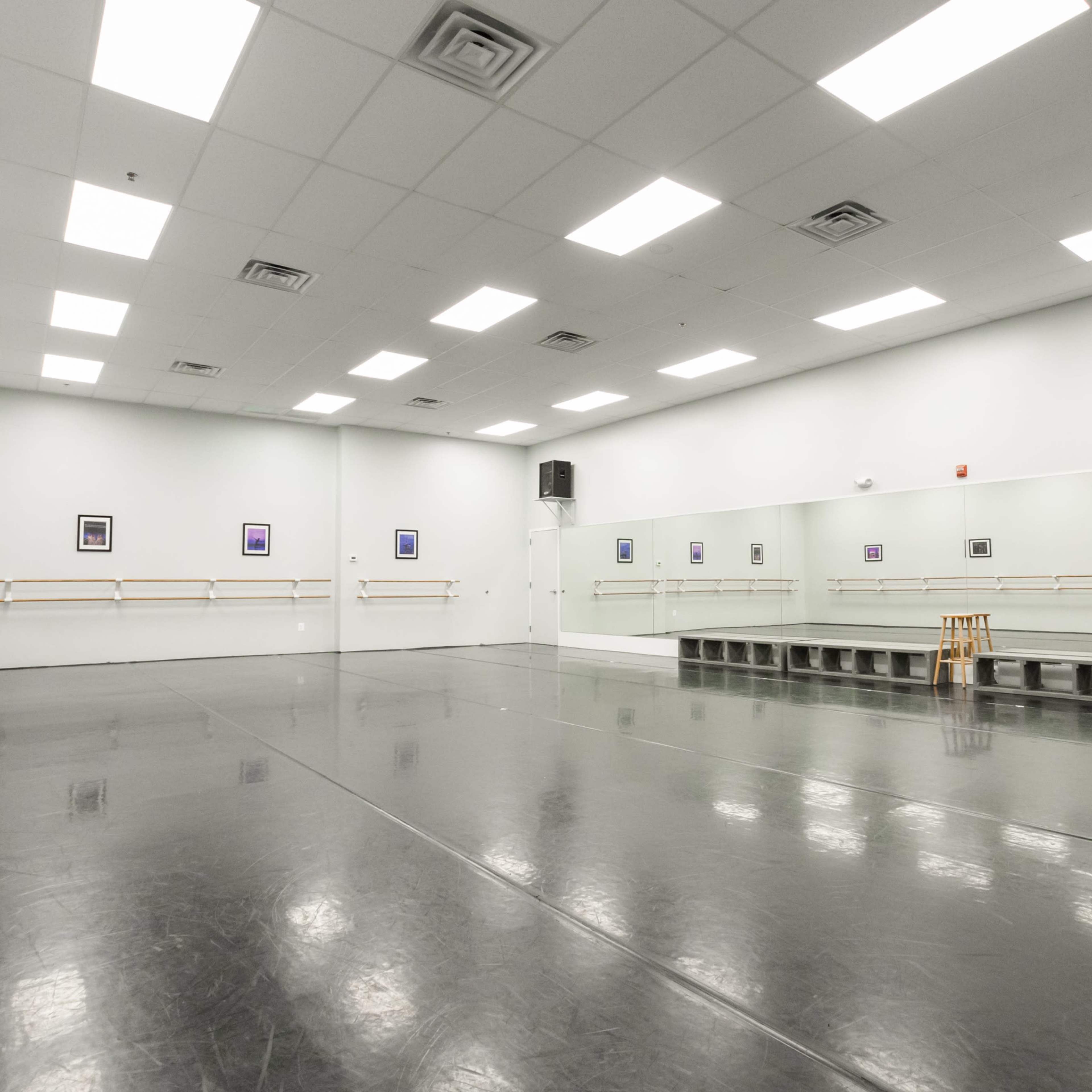 A spacious dance studio featuring a mirrored wall, wooden barre, and a small raised platform.