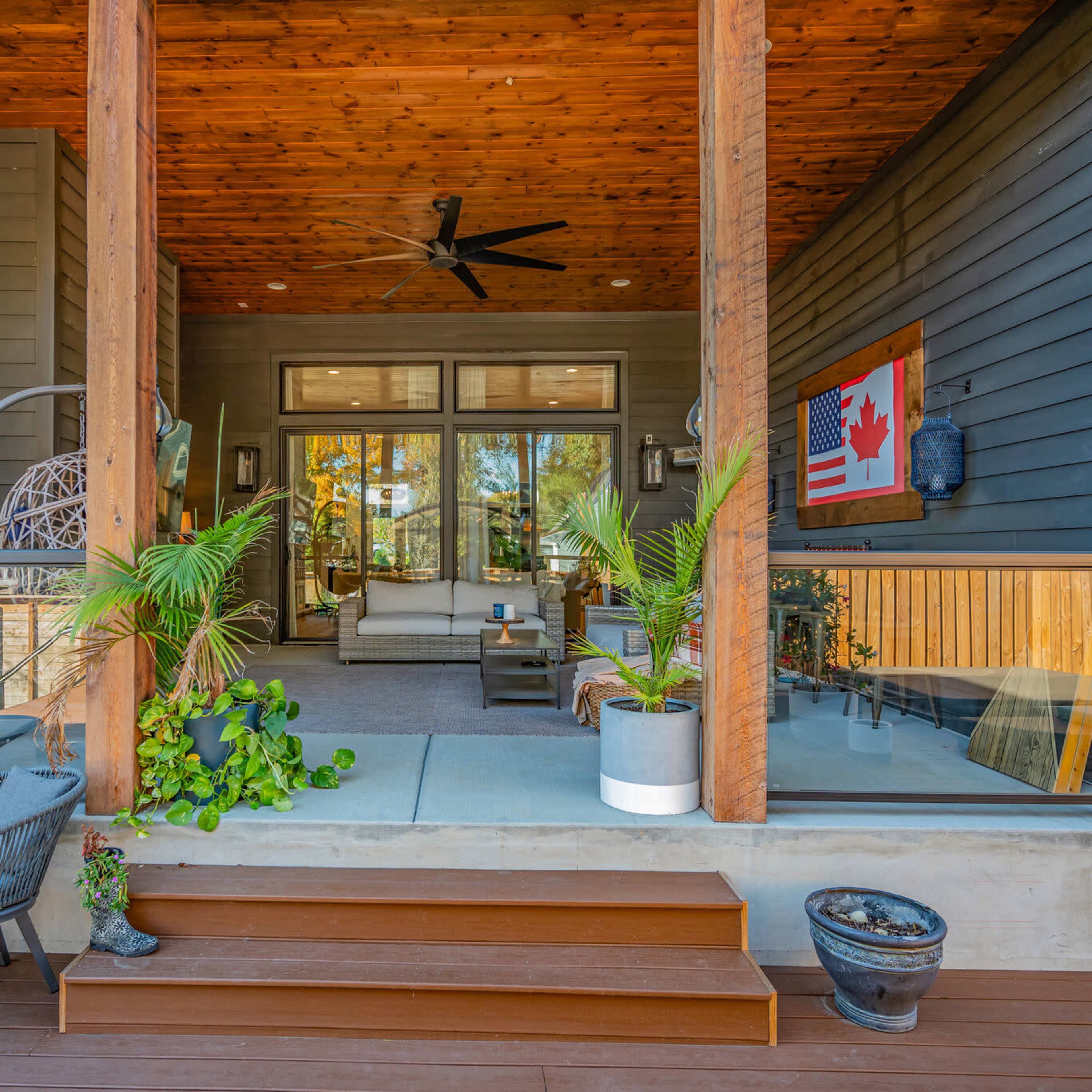 A covered patio with wooden beams, featuring a seating area with a sofa and plants, and steps leading to the outdoor space.