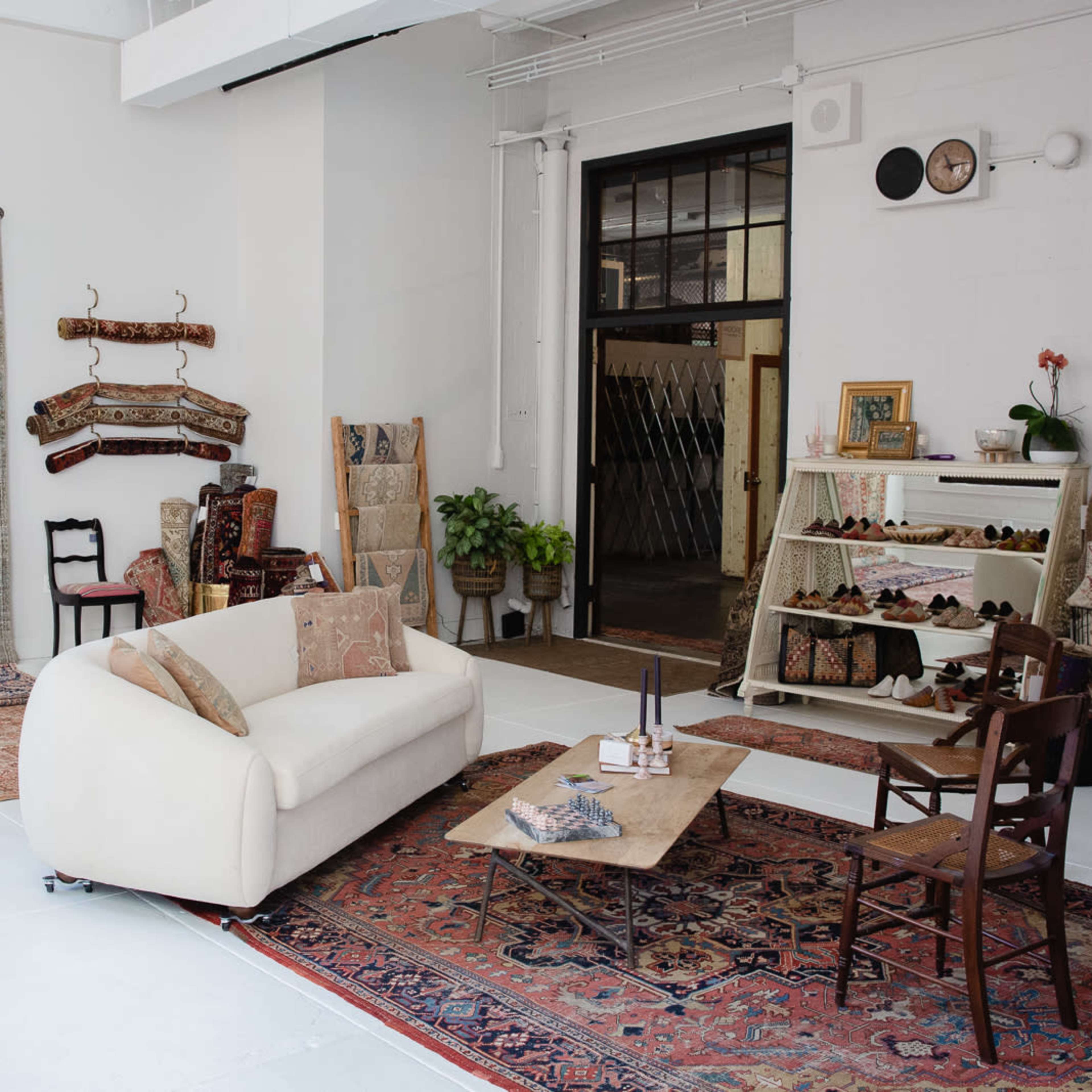 A spacious interior with a white couch, a wooden coffee table, shelves displaying items, and several patterned rugs on the floor.