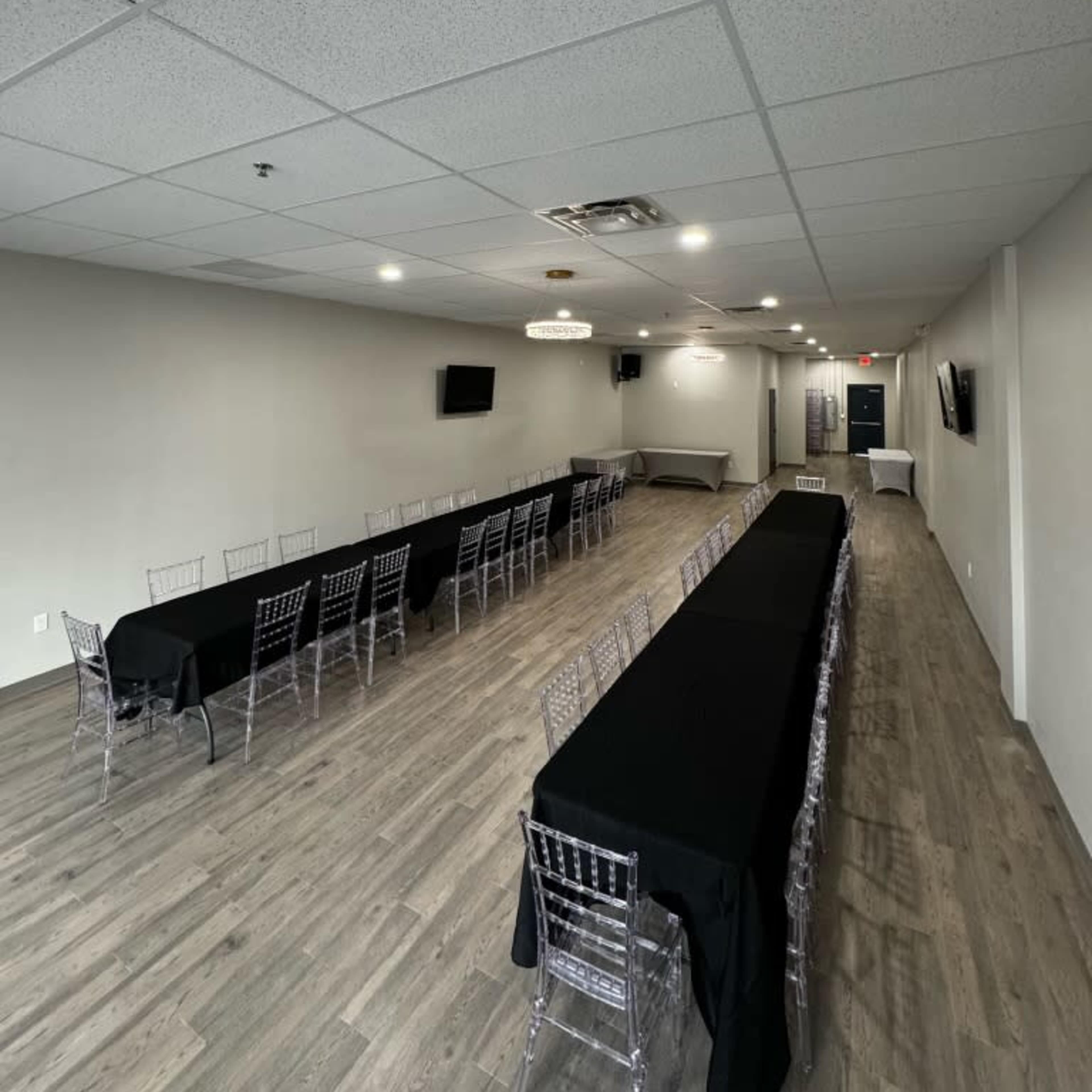 A modern event space features long tables with black tablecloths set up in a well-lit room with a wooden floor and minimal decor.