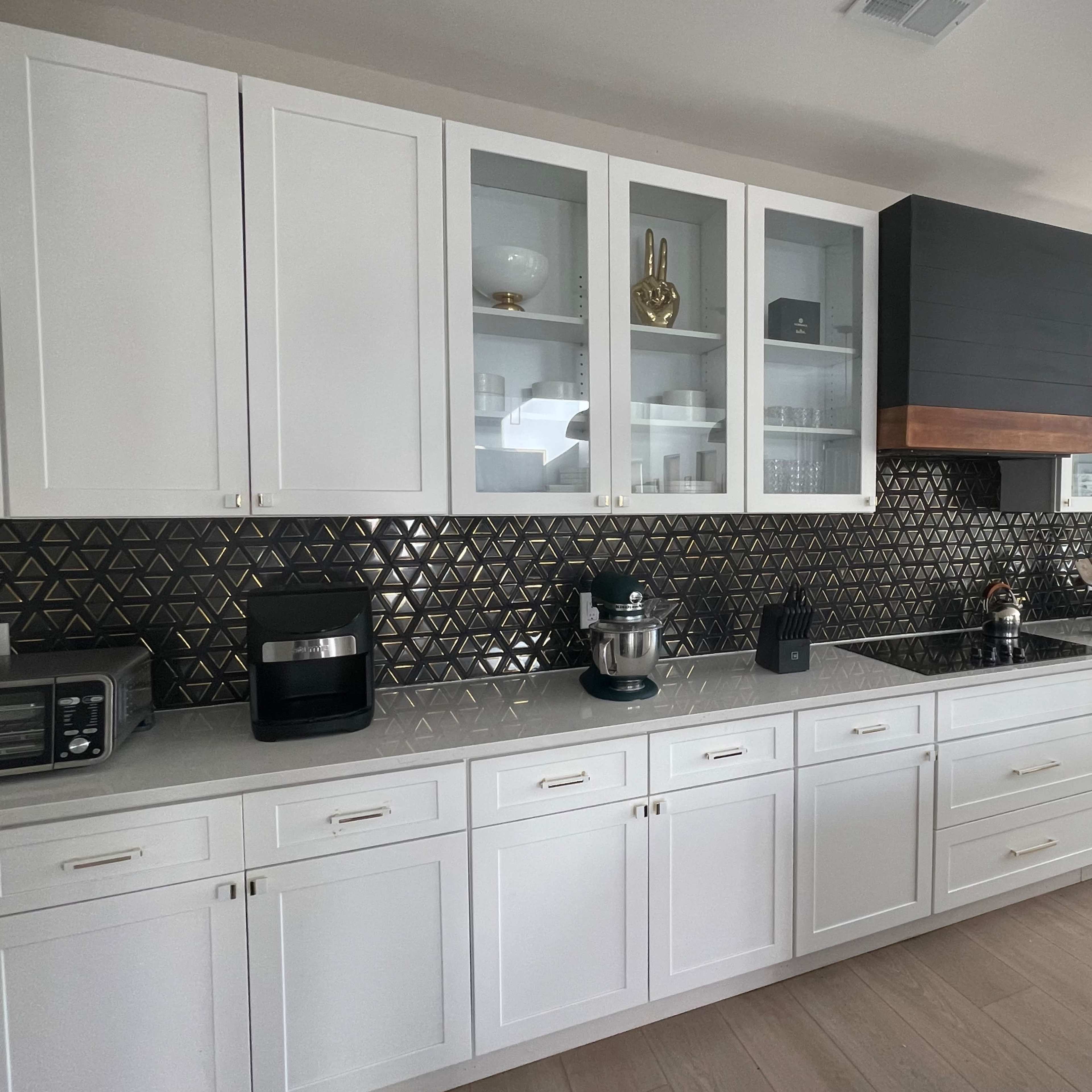 The kitchen features white cabinetry, a black tiled backsplash with a geometric pattern, and modern appliances including a toaster and a stand mixer.