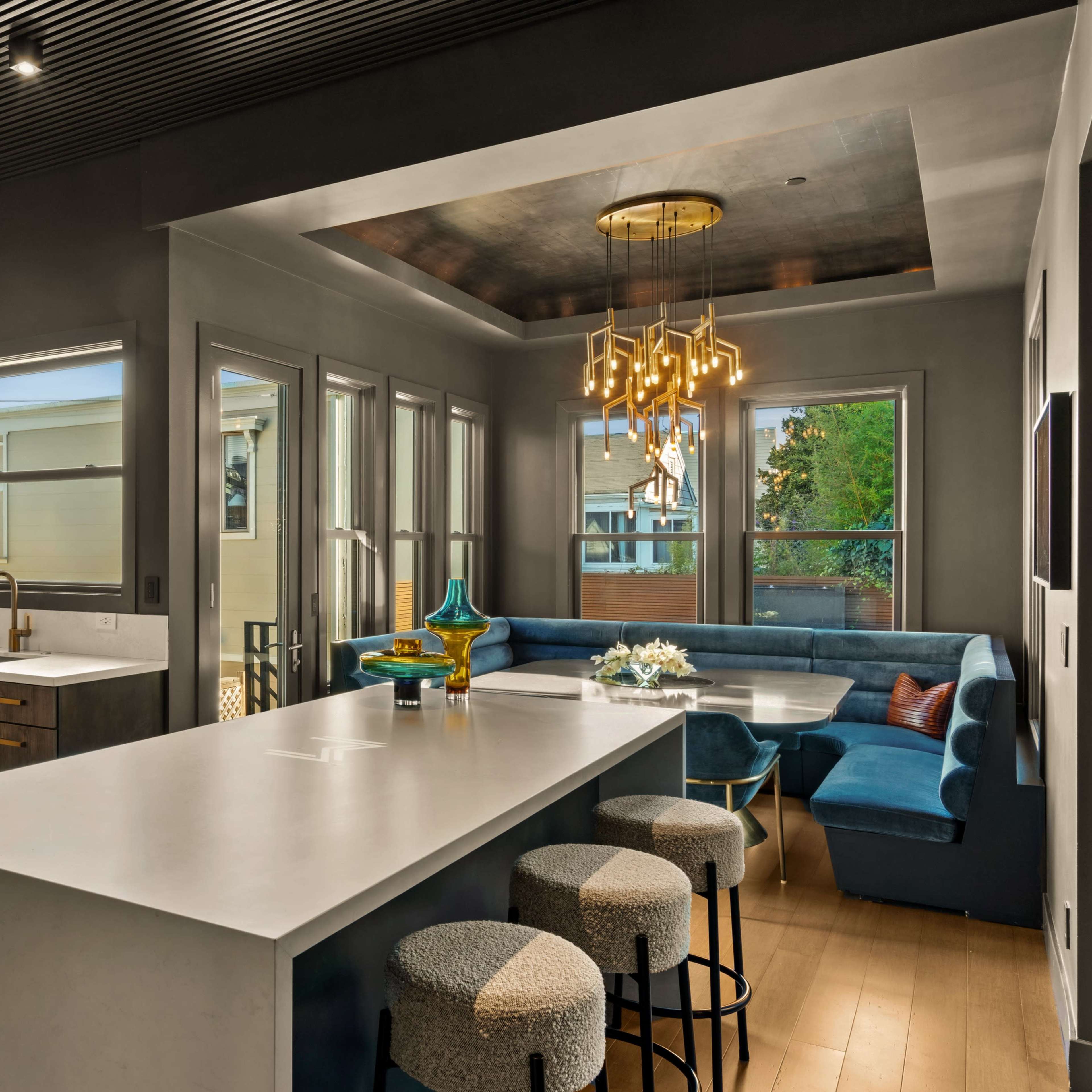 A modern kitchen with a large island, a stainless steel stove, wooden cabinets, and a blue seating area with a table.