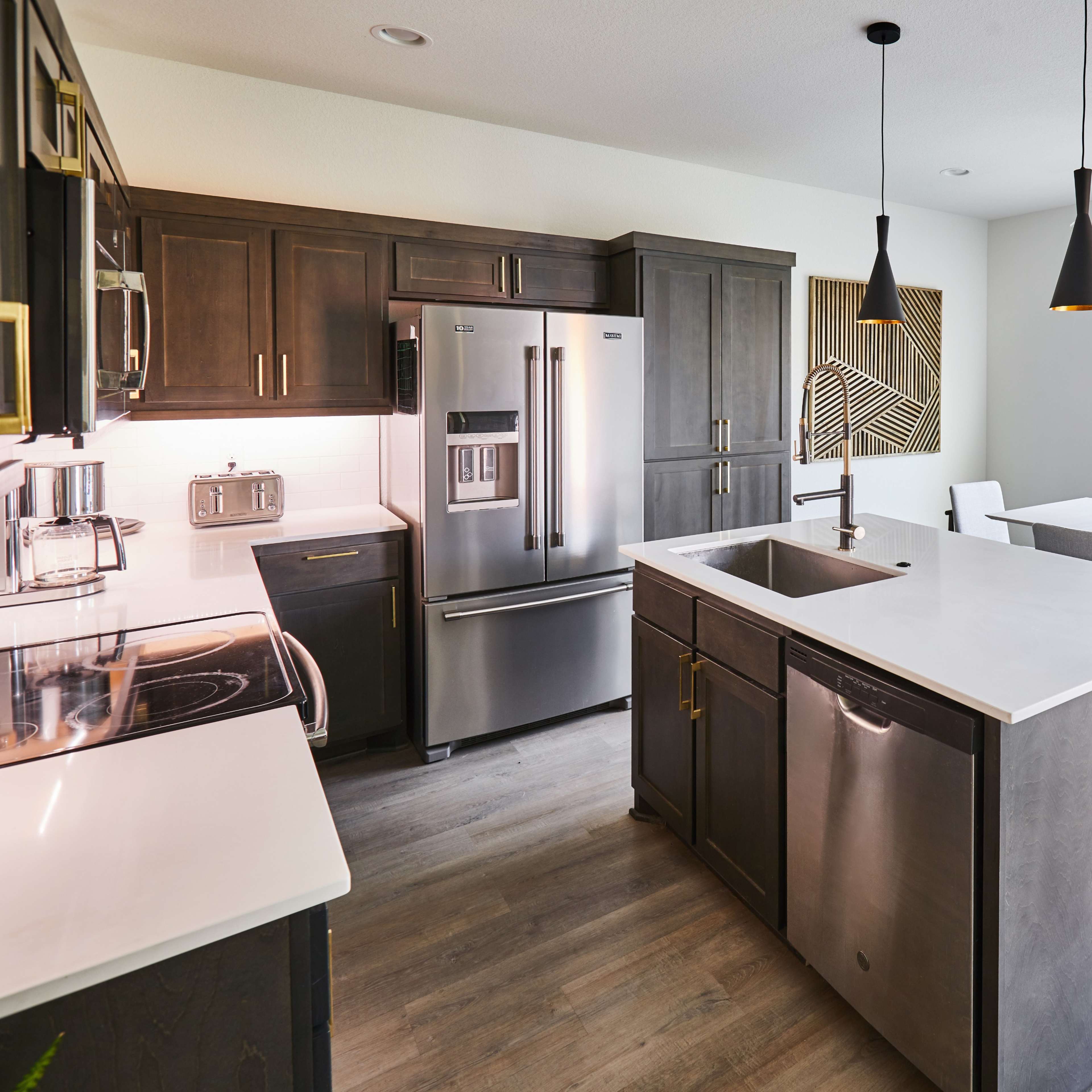 A modern kitchen featuring dark wood cabinets, stainless steel appliances, and a white countertop with an adjacent dining area.