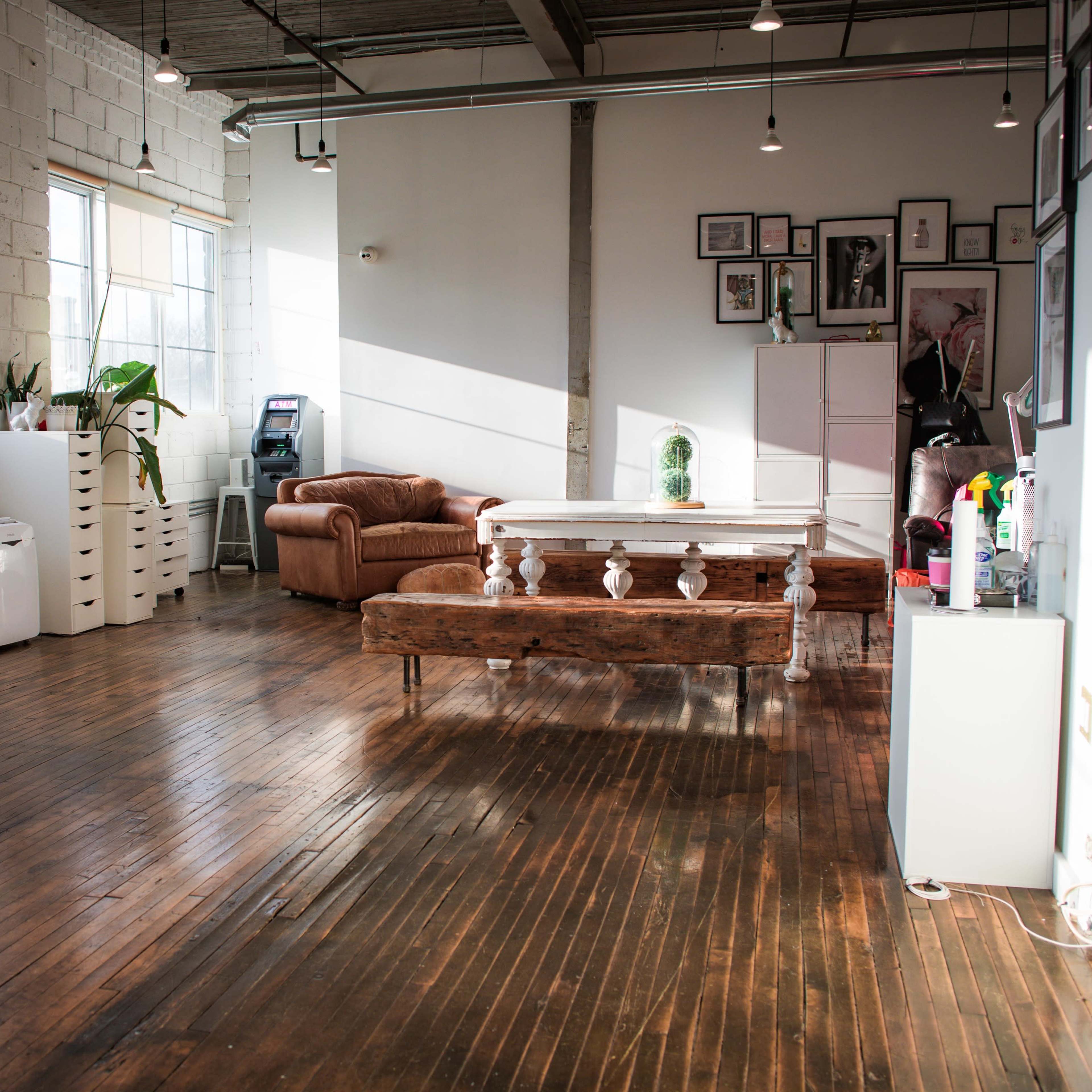 A spacious, brightly lit room with wooden floors, a large table, a brown couch, and various decor on the walls.