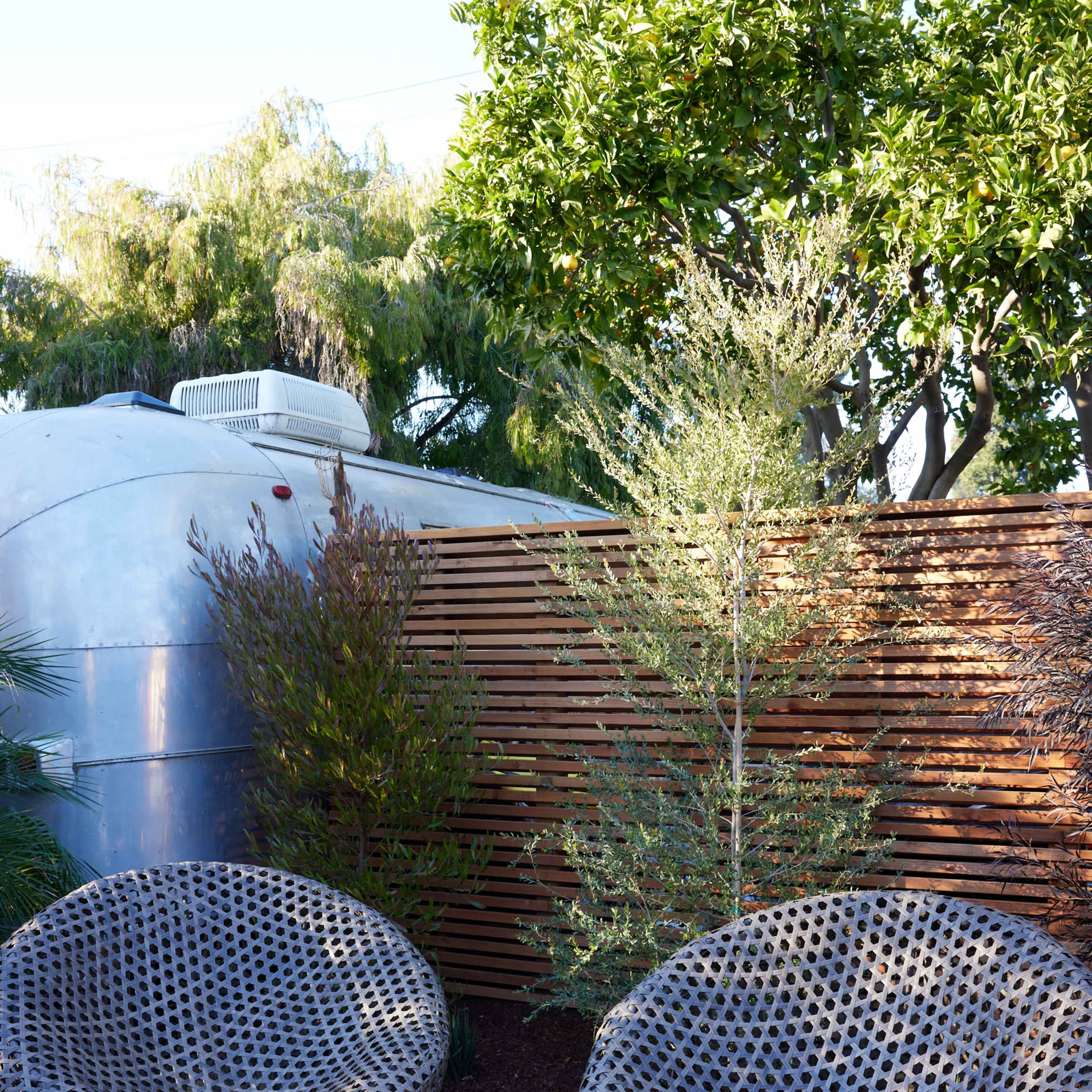 Two round, woven chairs placed on a gravel surface next to a wooden fence and lush greenery.