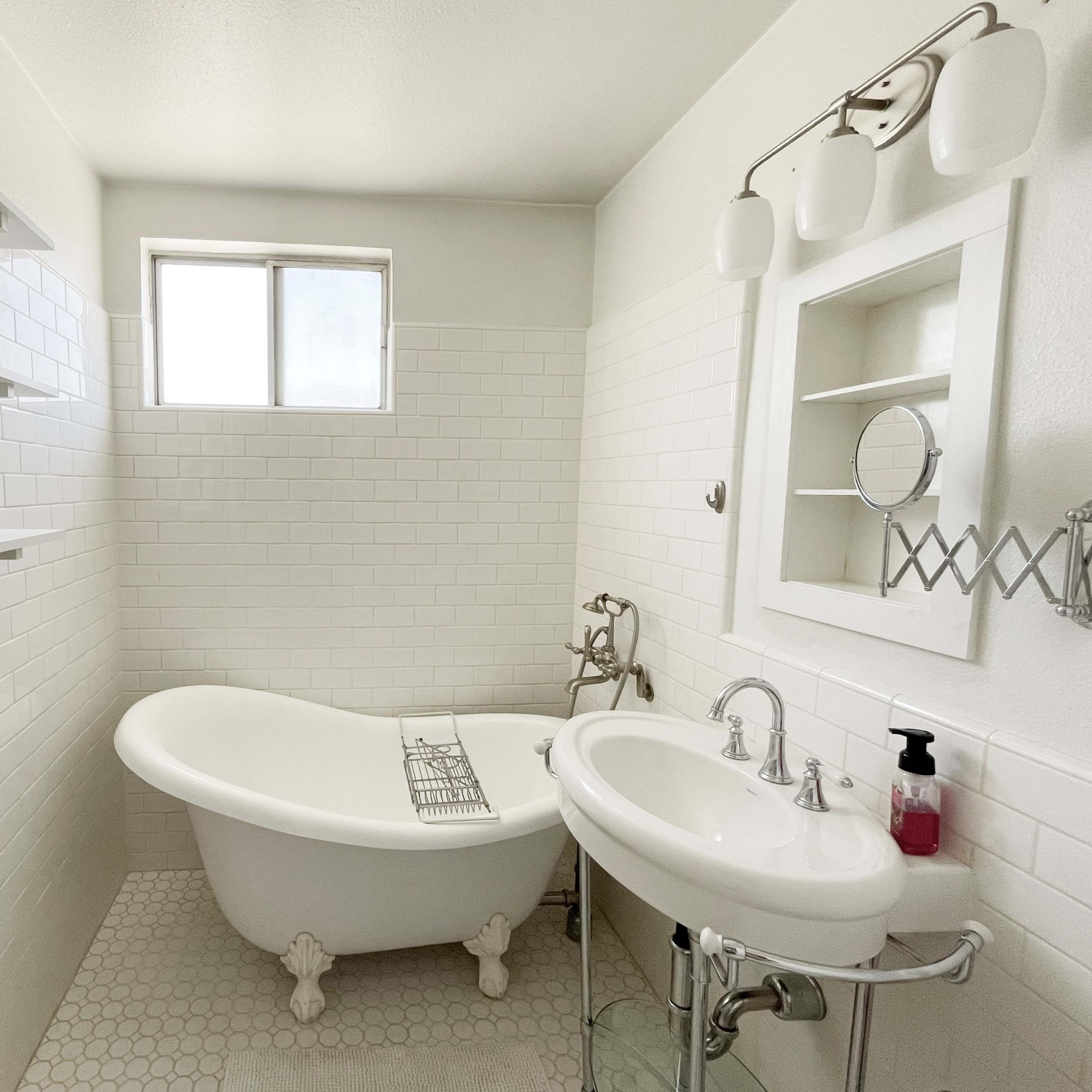 A bathroom featuring a freestanding bathtub, a sink, and tiled walls with a window allowing natural light.