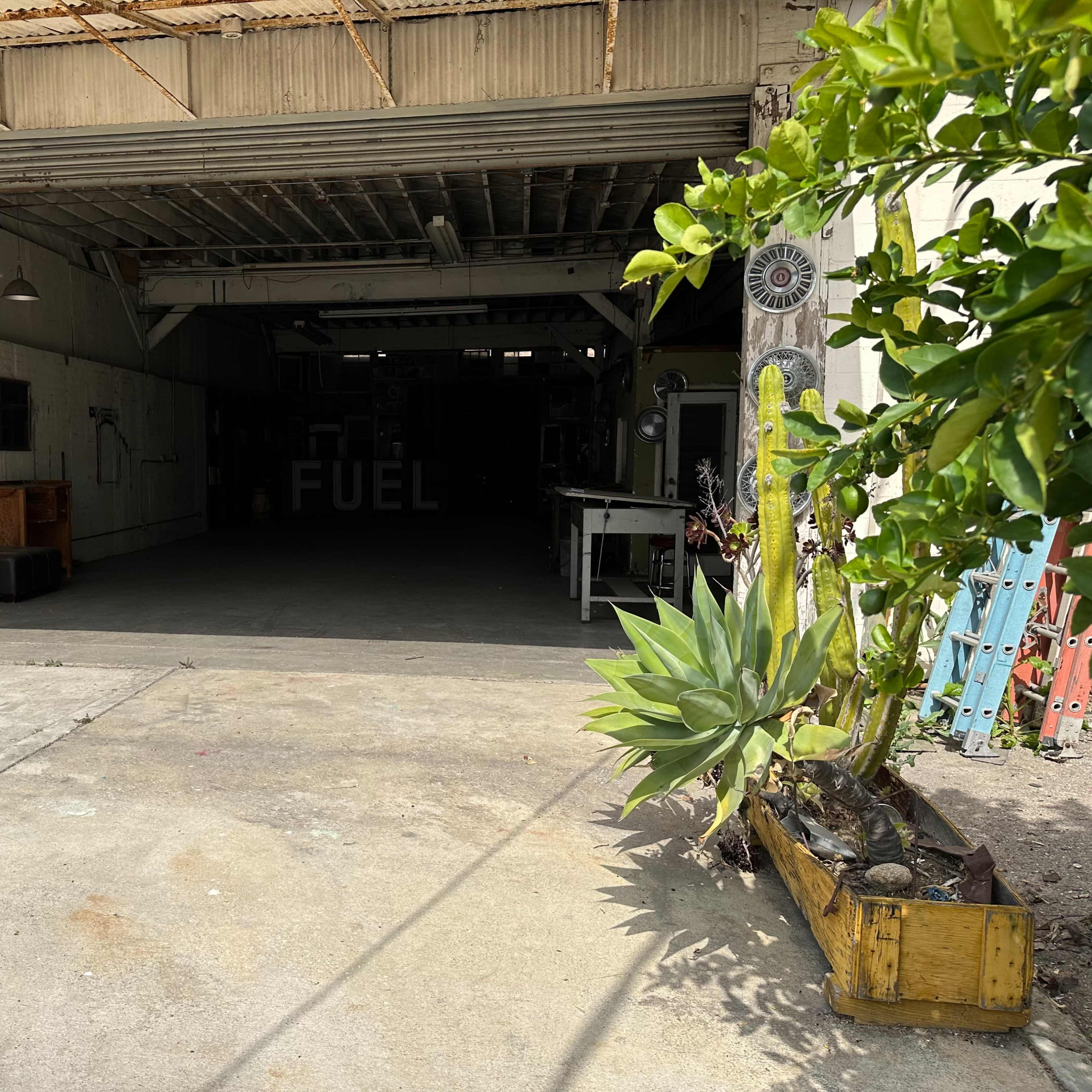 An open garage with a concrete floor, a potted plant in front, and the word "FUEL" visible on the back wall.