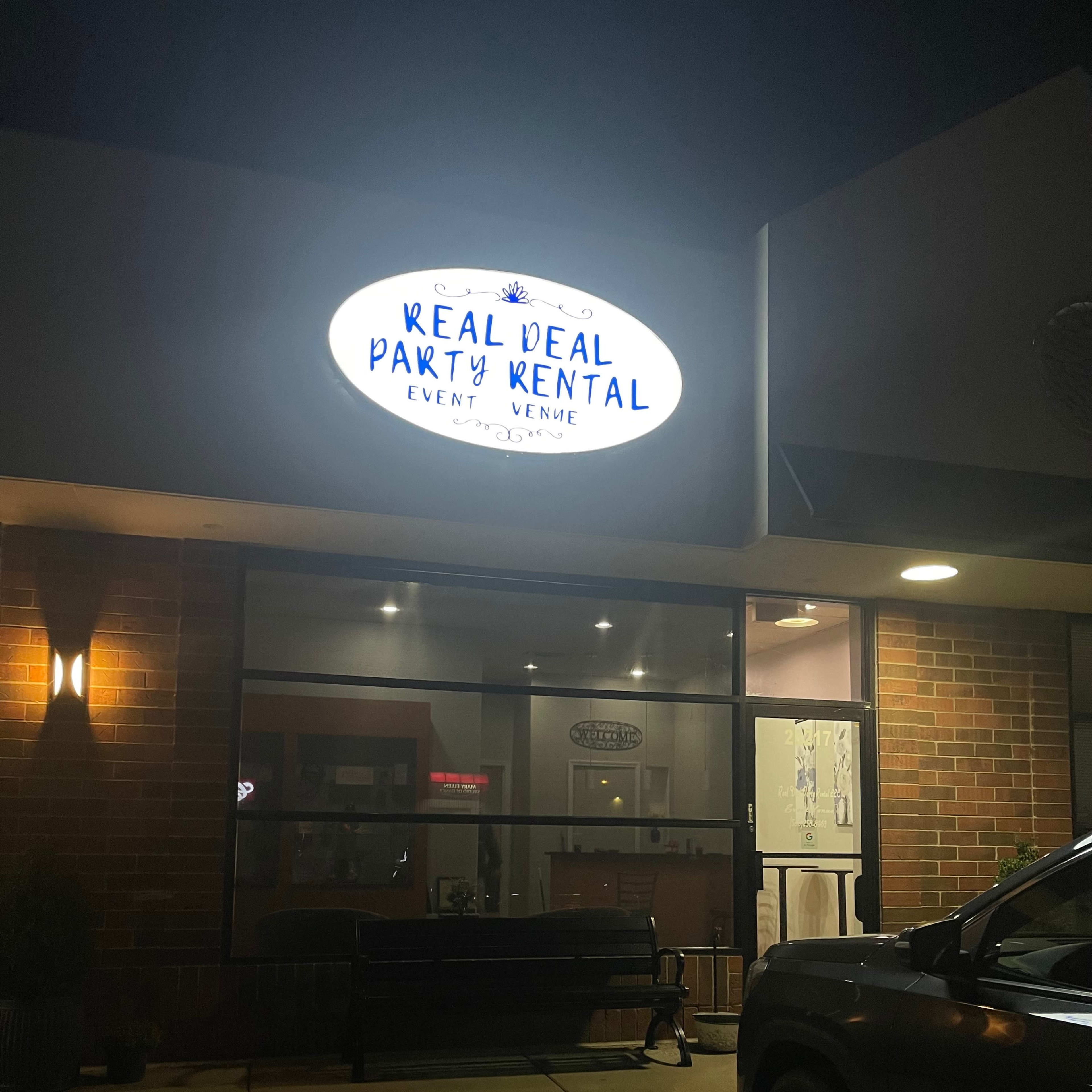 A dimly lit storefront with a sign reading "Real Deal Party Rental" displayed above the entrance.