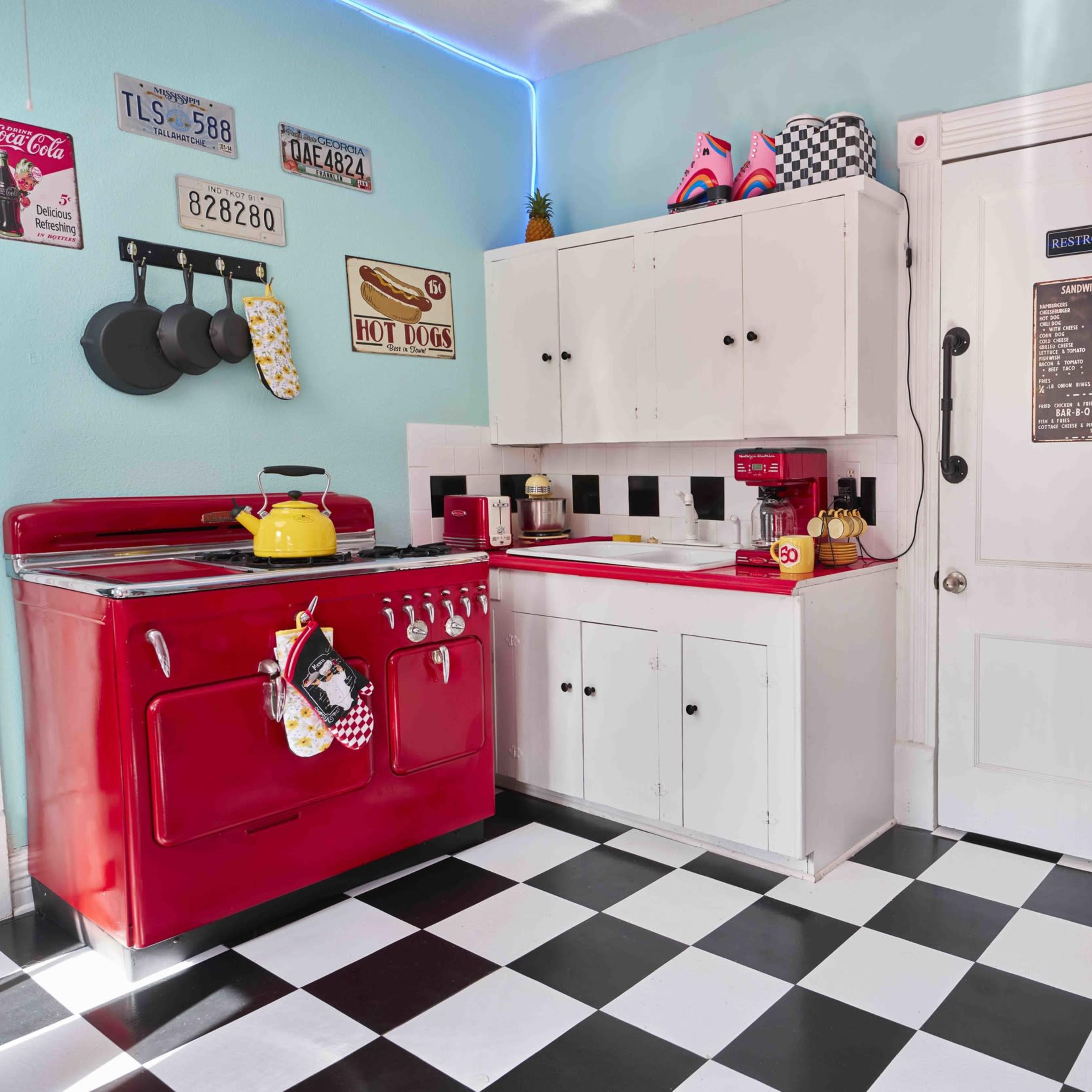 A retro-style kitchen featuring red appliances, black and white checkered flooring, and white cabinetry.