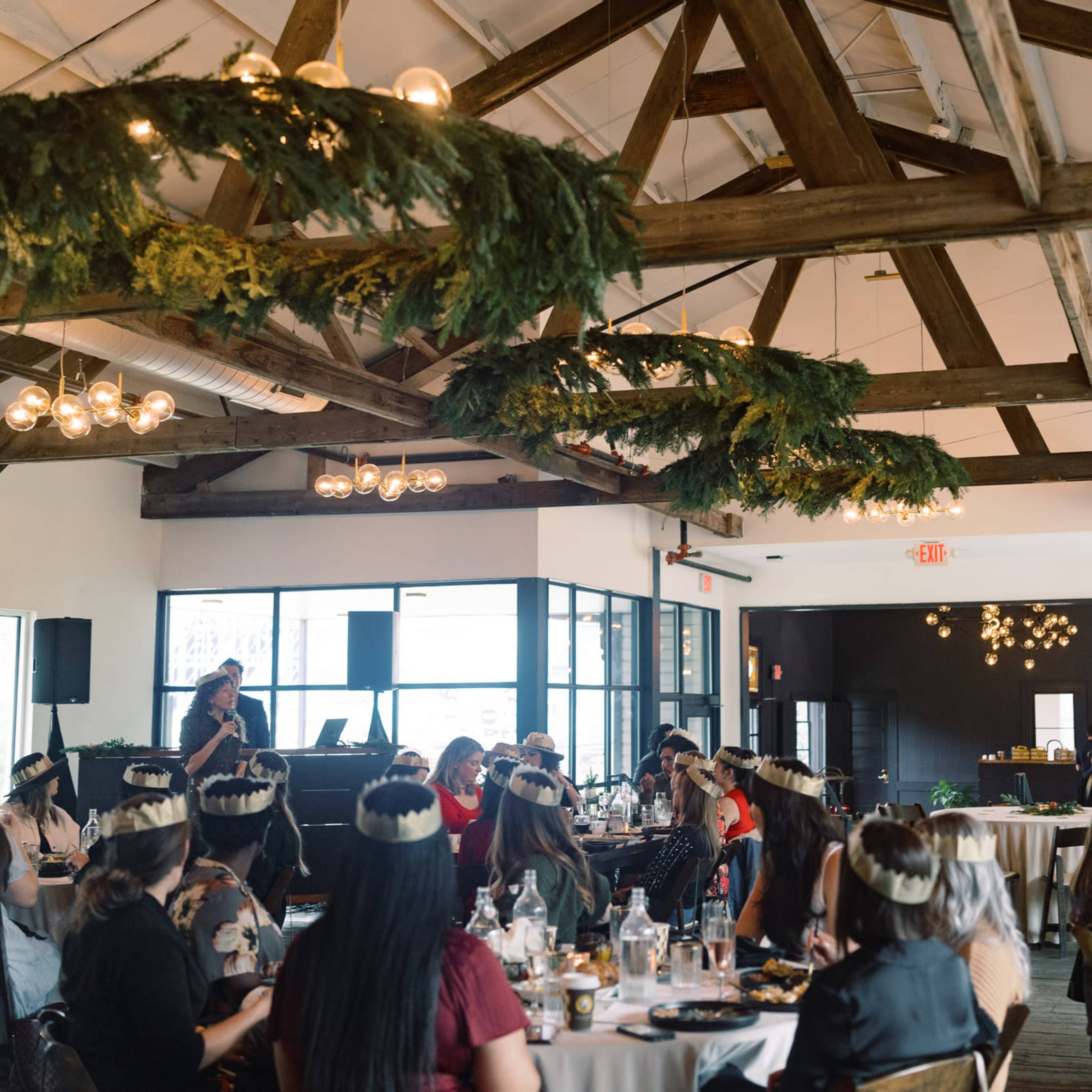A large audience listens to a speaker at a panel event featuring a decorative stage with floral elements and branding.