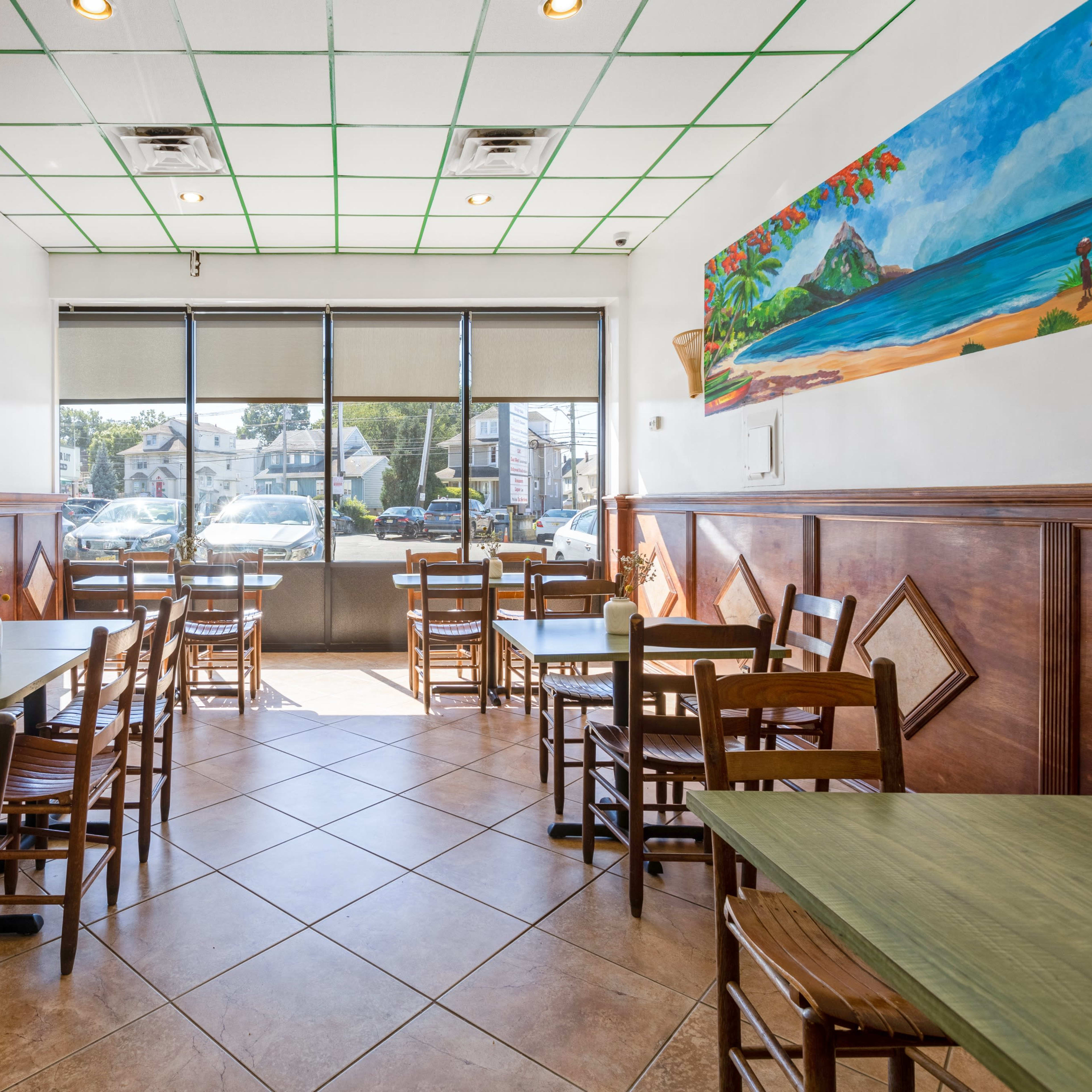A café interior with empty tables and chairs arranged in a bright space featuring large windows and a mural of a beach scene on the wall.