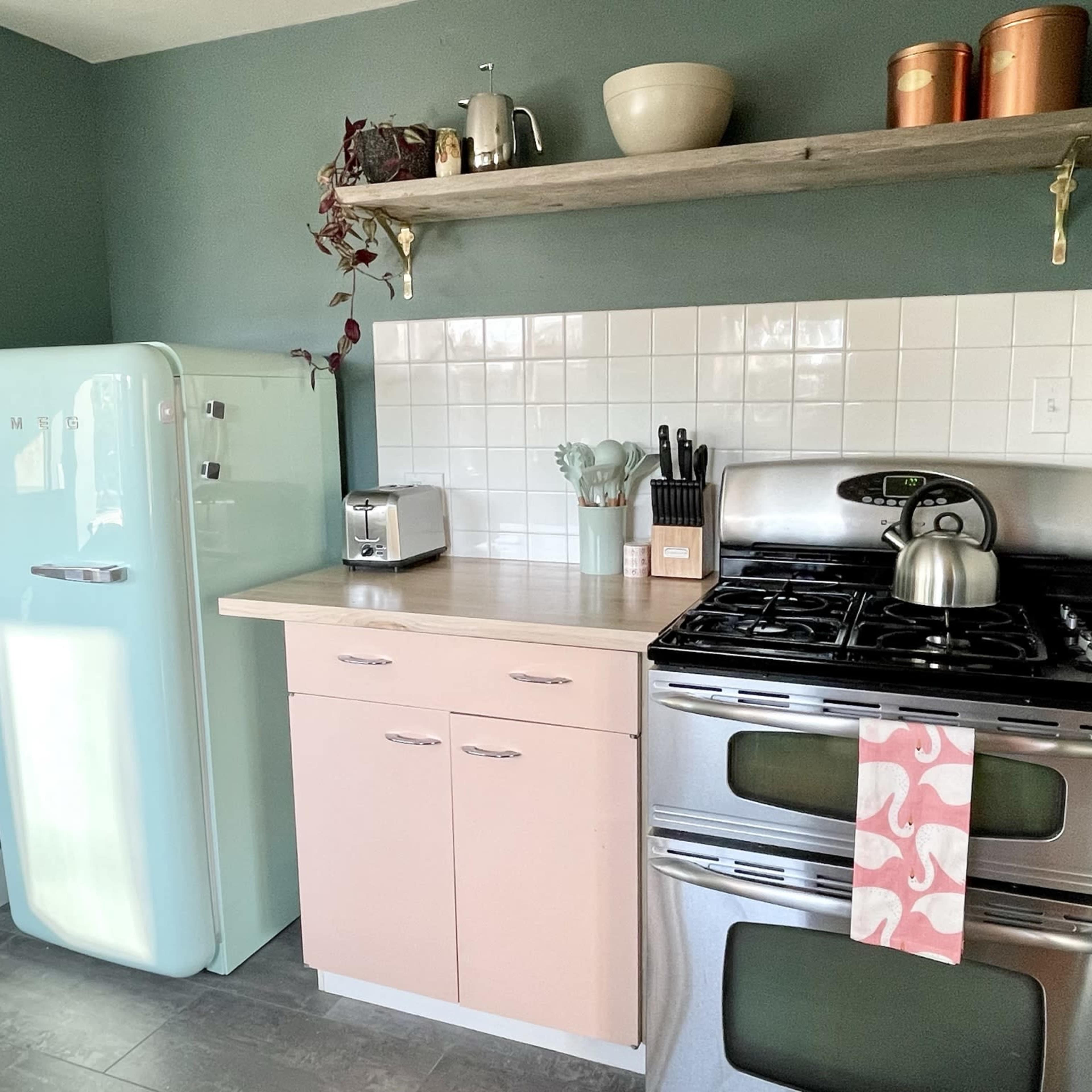 A kitchen with a vintage-style light blue refrigerator, a modern stainless steel stove, a wooden shelf, and various kitchen utensils arranged on the countertop.