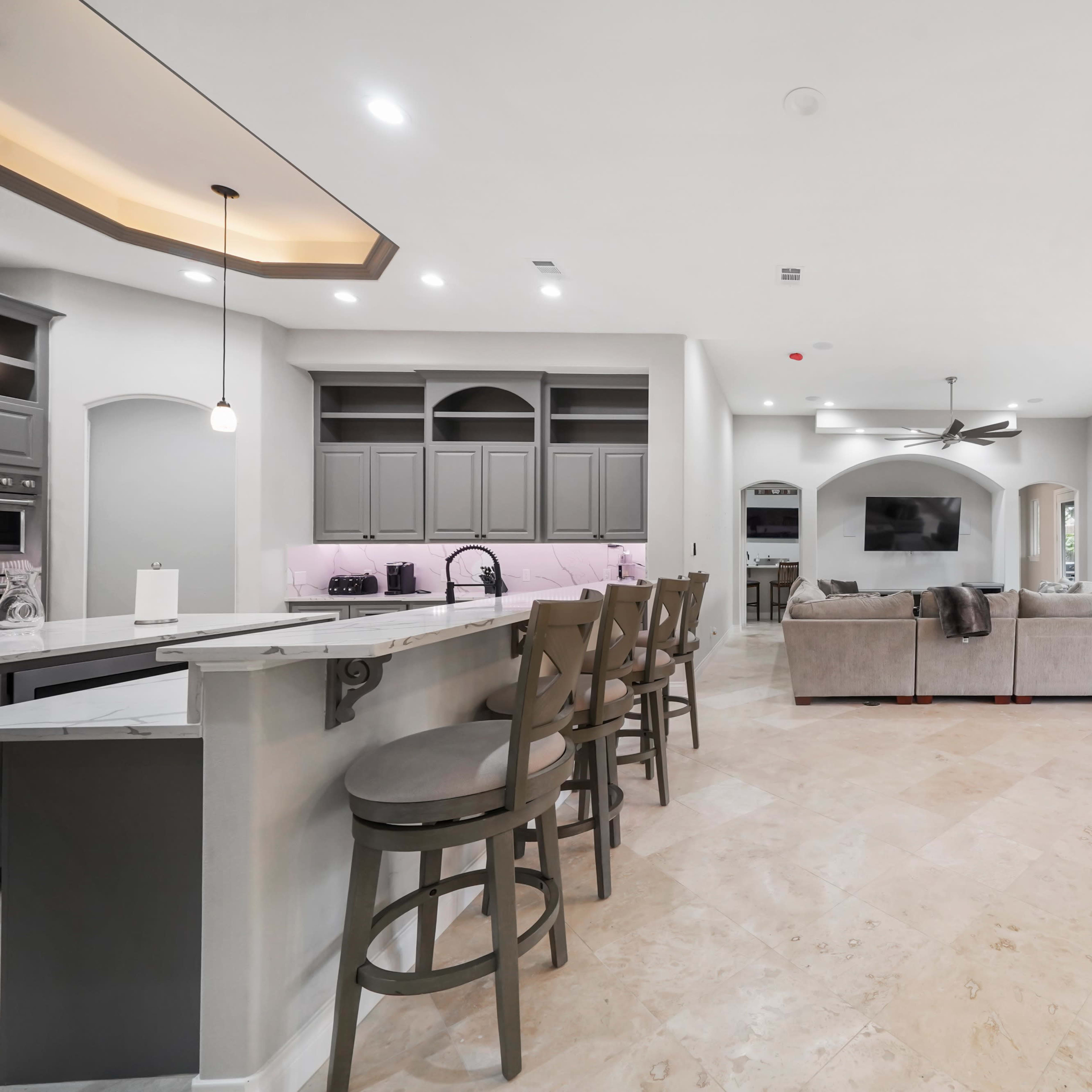 A spacious modern kitchen and living area featuring a breakfast bar, comfortable seating, and large windows allowing natural light.