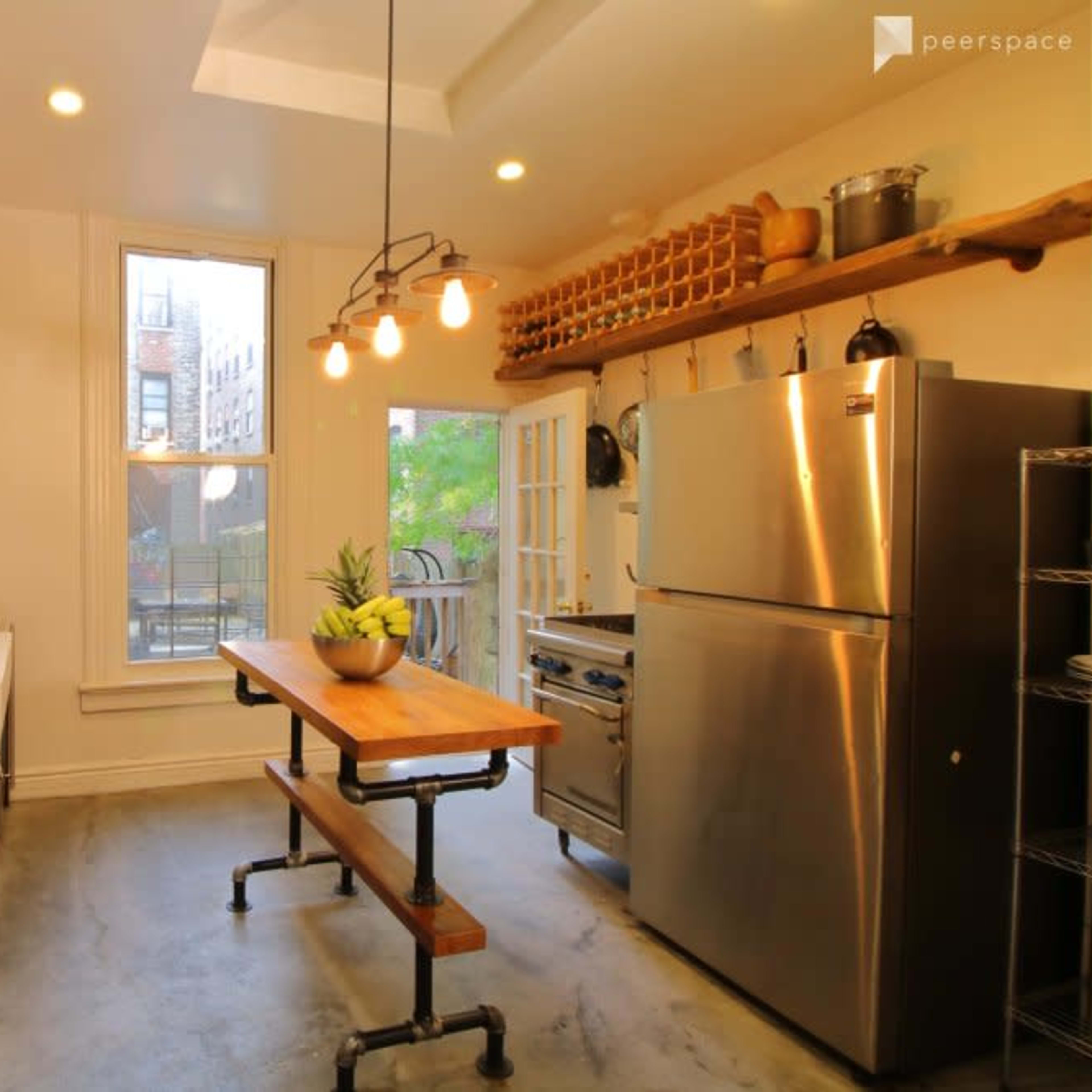 A modern kitchen featuring a stainless steel refrigerator, a wooden table, open shelving, and a large window providing natural light.