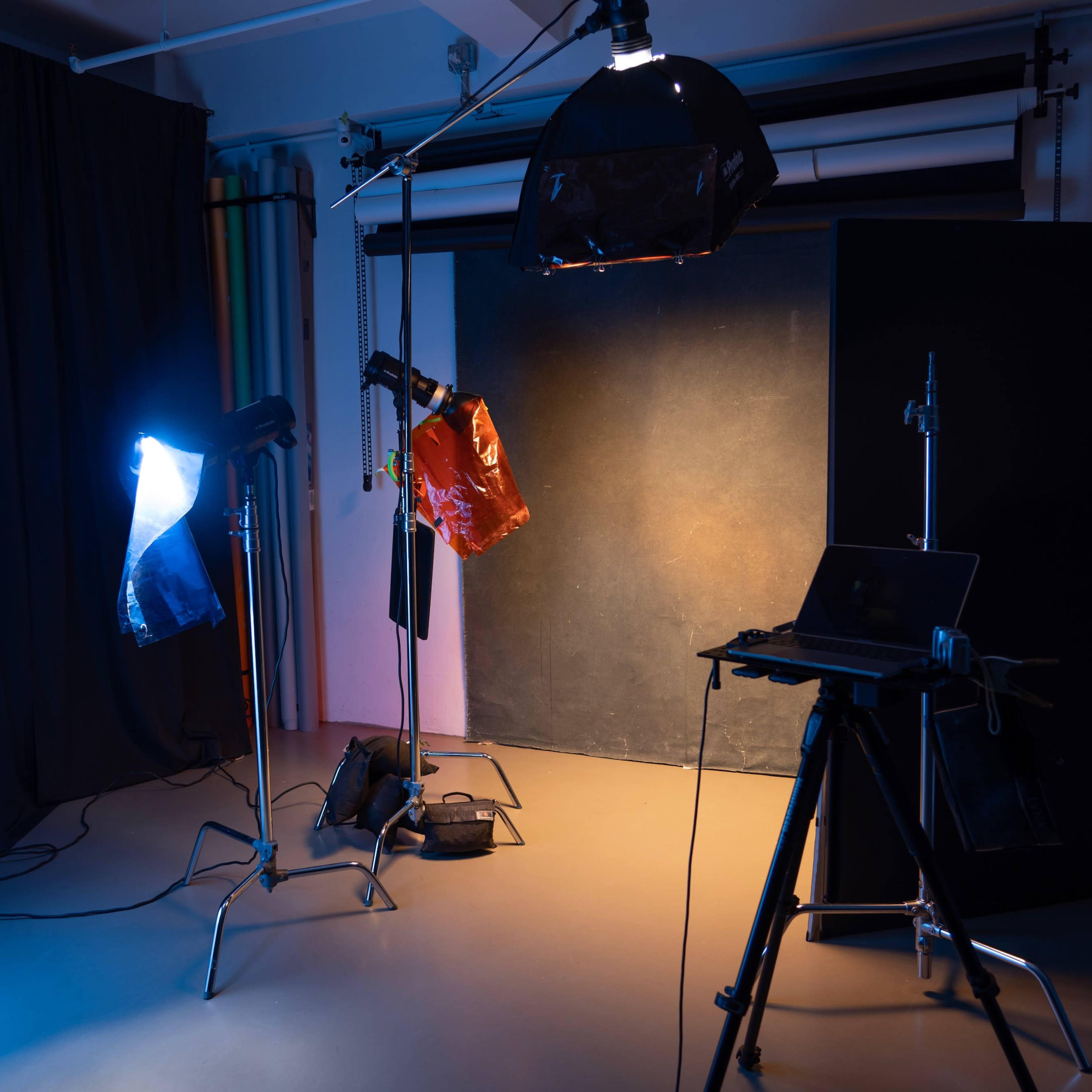 A photography studio setup with multiple lighting sources, backdrops, and a laptop on a tripod.