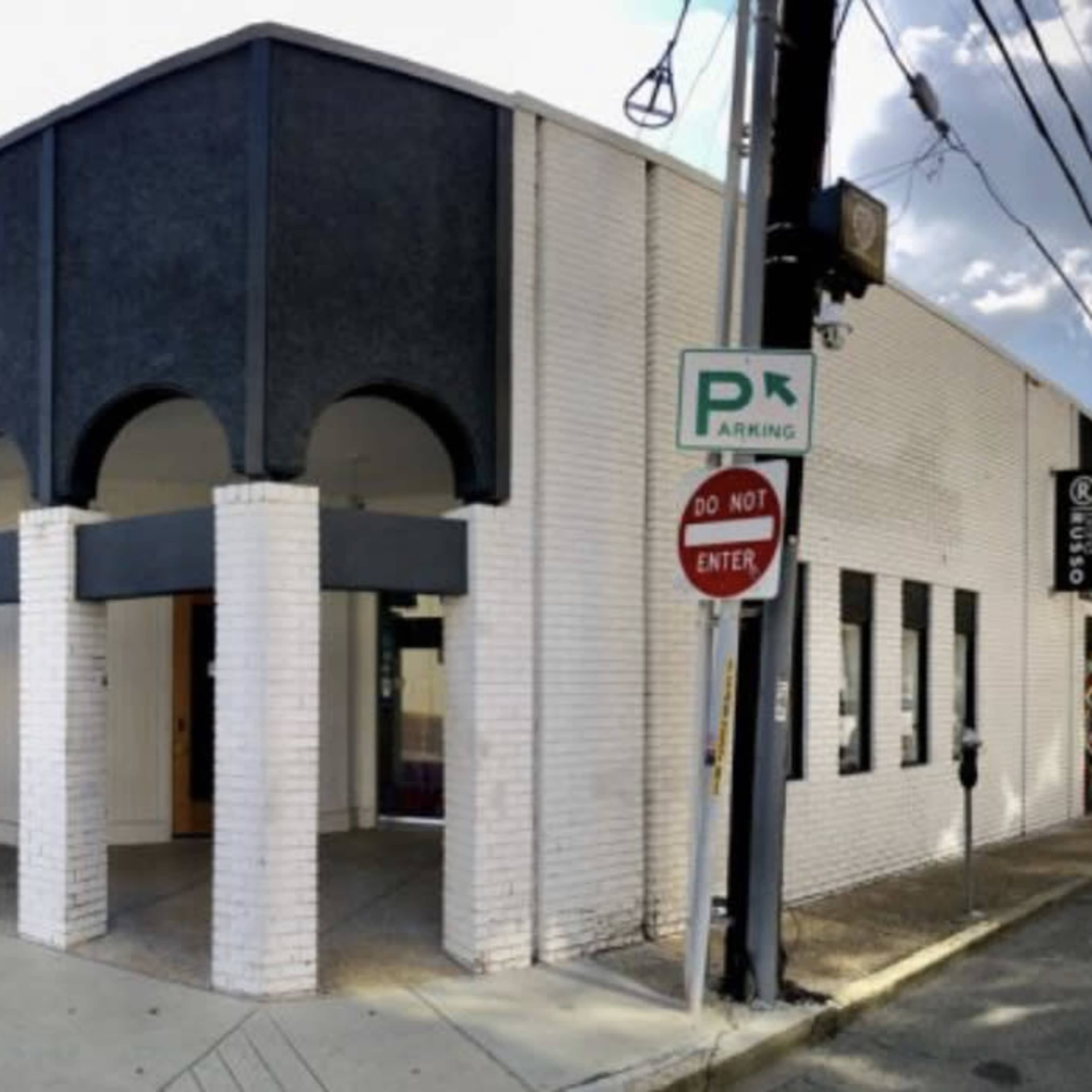 A modern, white brick building with a black, arched facade and large entrance, located at a street corner.