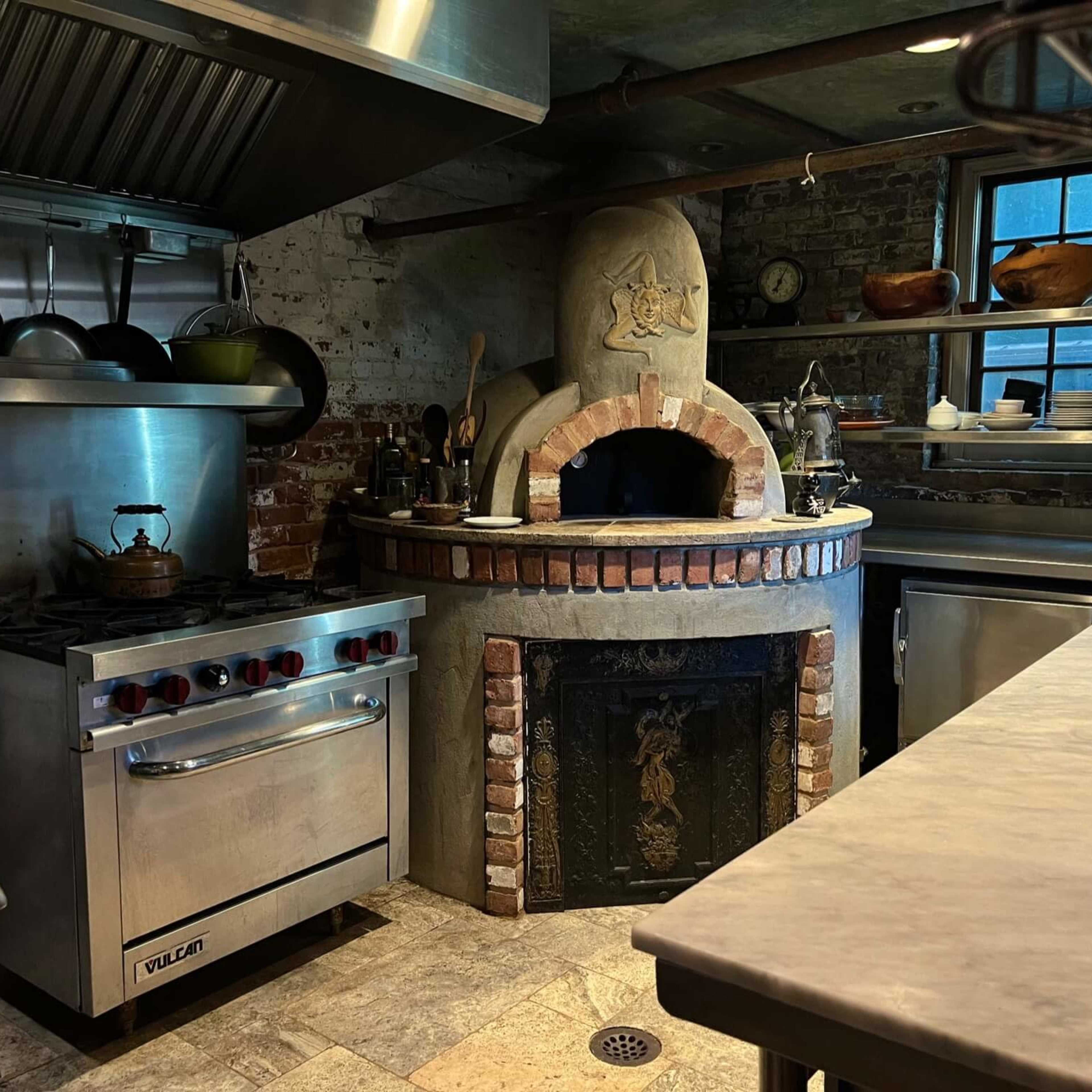 A rustic kitchen with a stone oven, stainless steel appliances, and exposed brick walls.