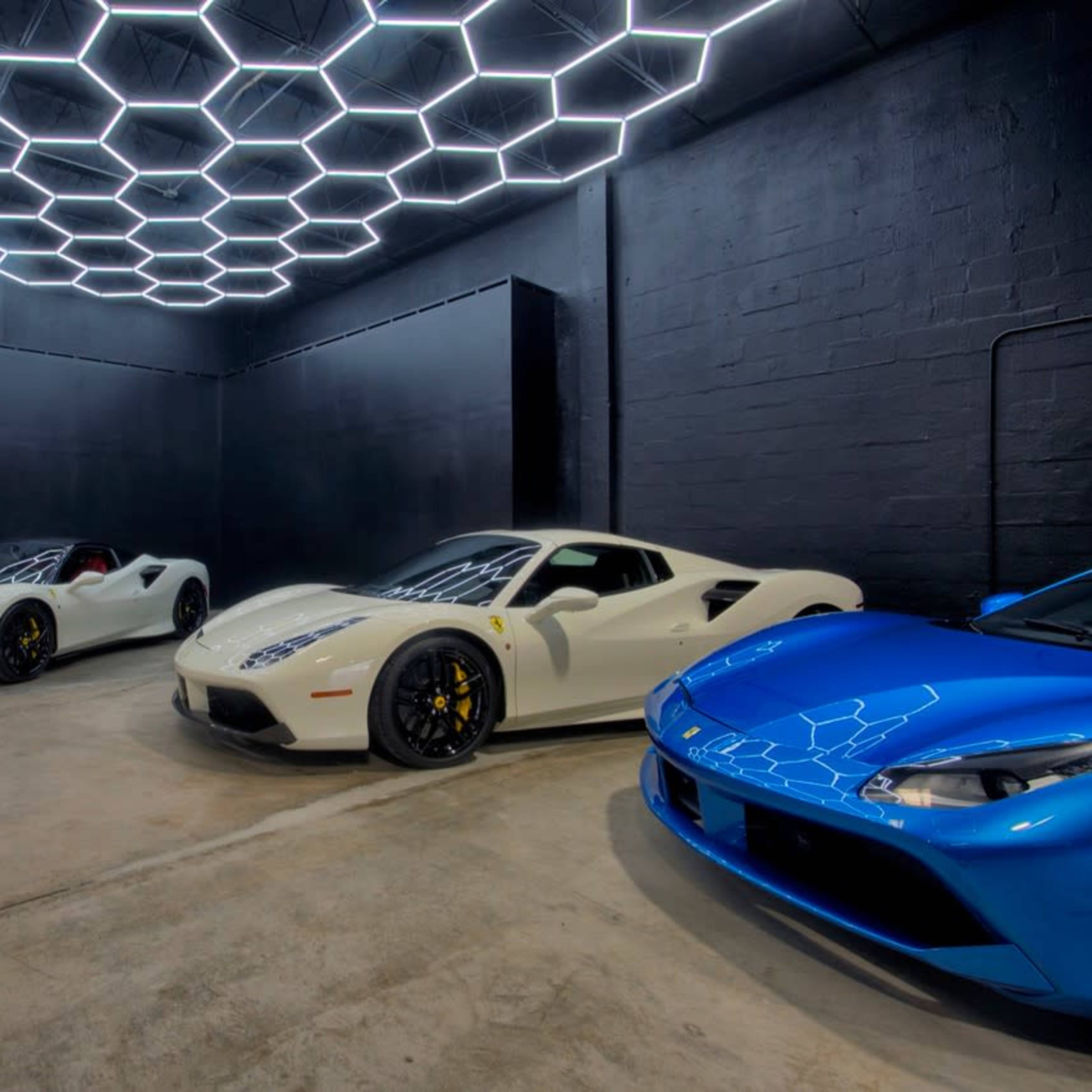 A modern garage featuring four luxury cars under a hexagonal LED light ceiling.