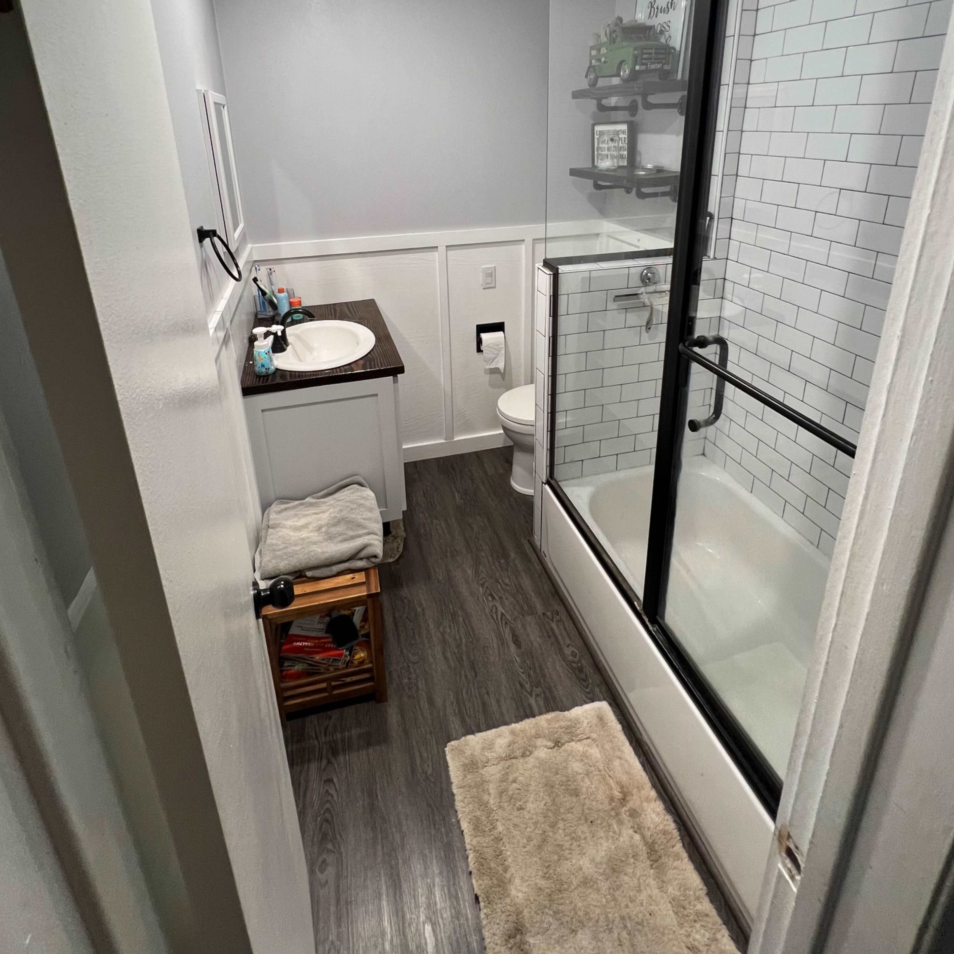 A bathroom with a shower and tub combination, a vanity with a sink, a toilet, and shelves for storage.