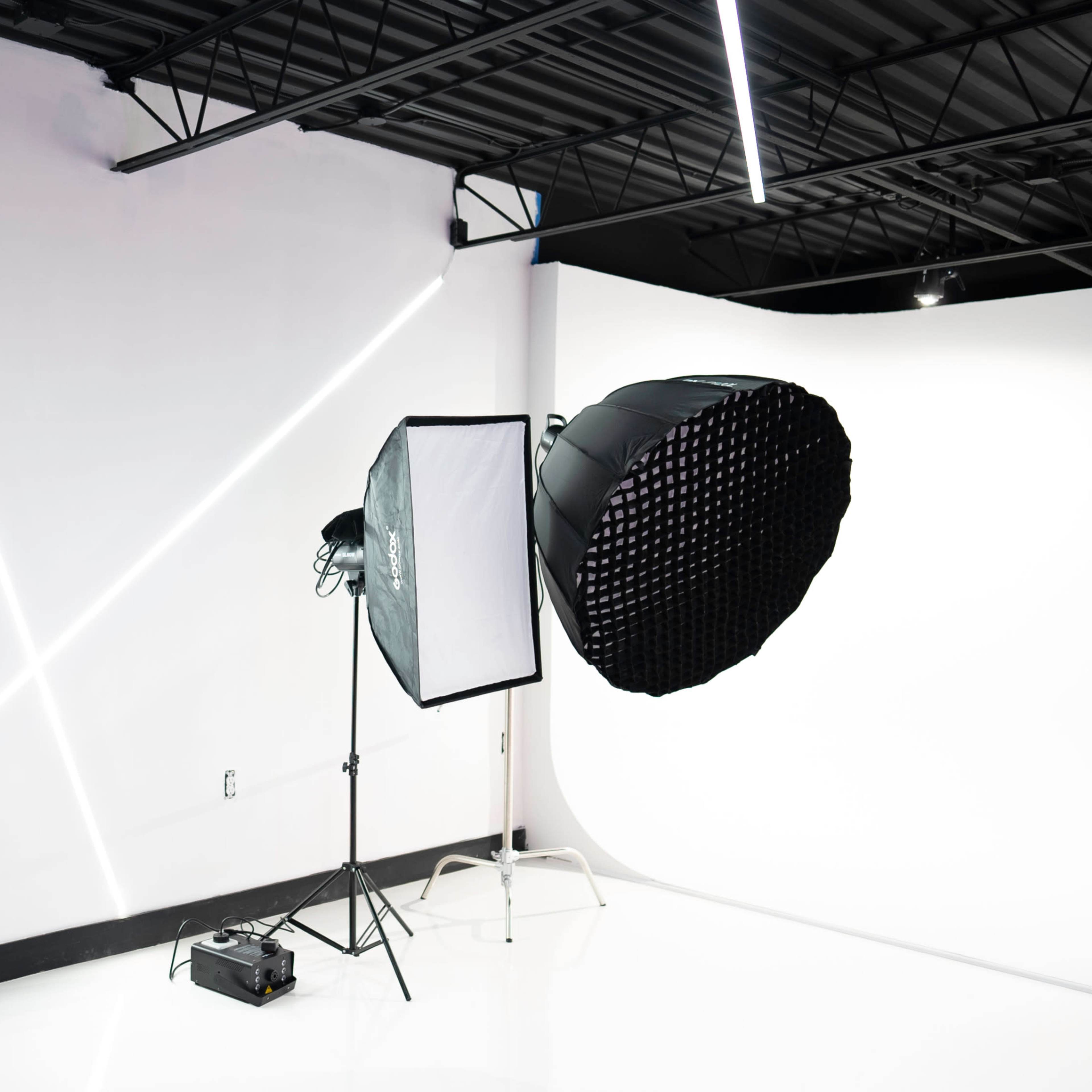 A photography studio with a large softbox light and a grid light set up against a white backdrop, illuminated by modern linear lights on the walls.